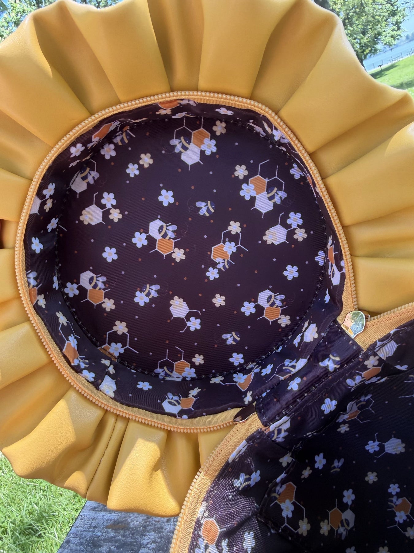 Close-up of the custom interior lining inside a honey jar shaped crossbody bag, featuring an exclusive bee, honeycomb, and white floral print on a rich brown background. The yellow ruffled bag opening frames the detailed pattern.