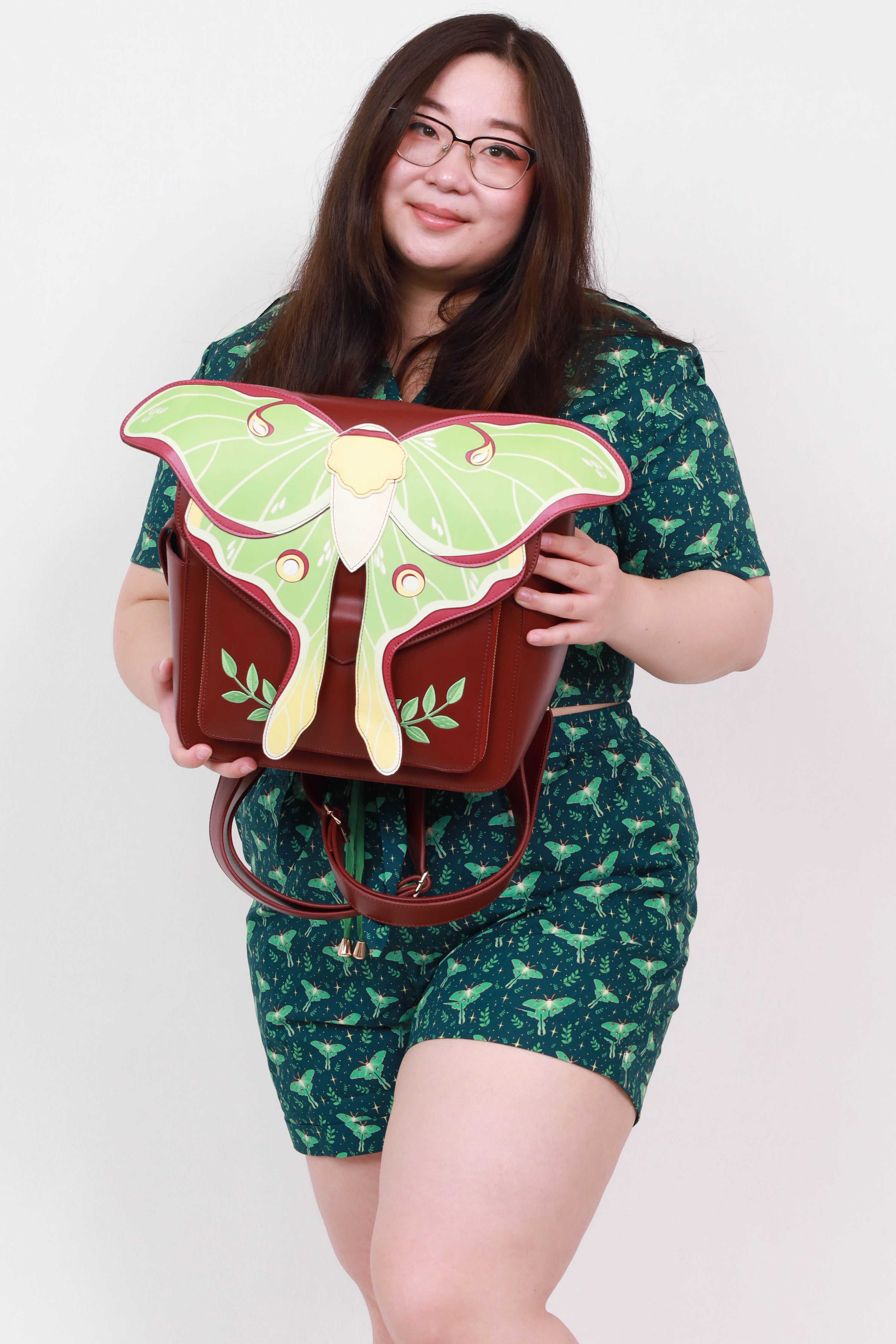 Model holding the Luna Moth Backpack featuring layered green luna moth wings, embroidered leaf details, and nature-inspired fantasy design.