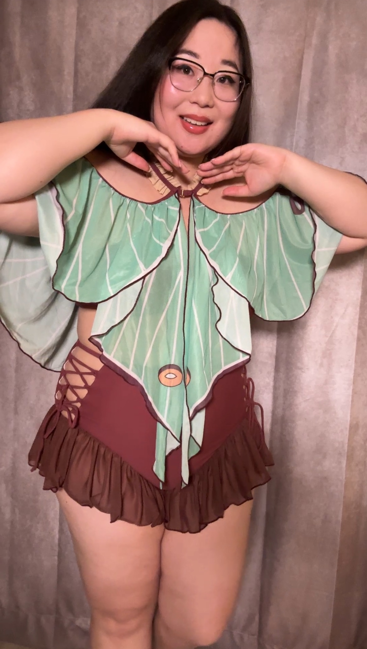 Model wearing a luna moth-inspired fairycore swimsuit prototype featuring green wing-like sleeves, lace-up details, and brown ruffled bottoms.
