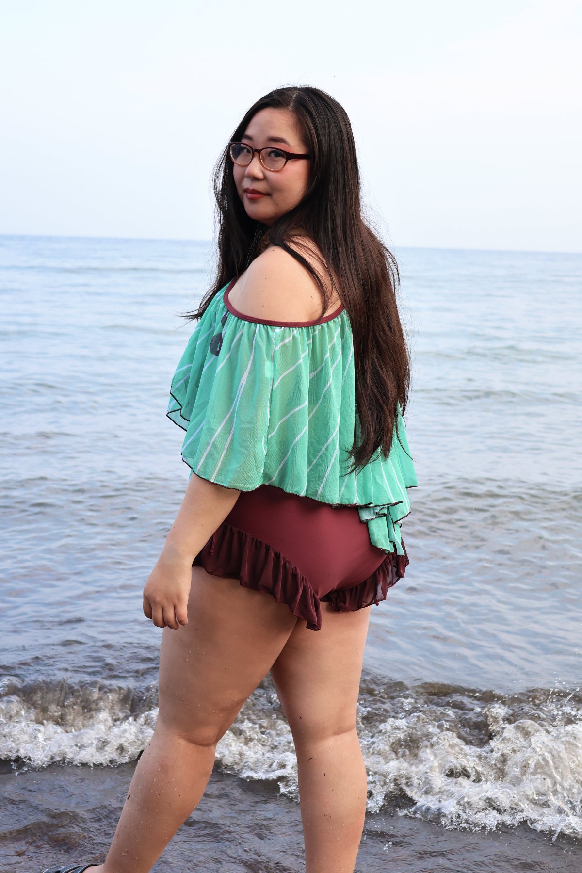 Back and side view of the Nyahallo Luna Moth Swimsuit featuring a flowing mint green moth wing-inspired cape and burgundy ruffle swimsuit at the beach.