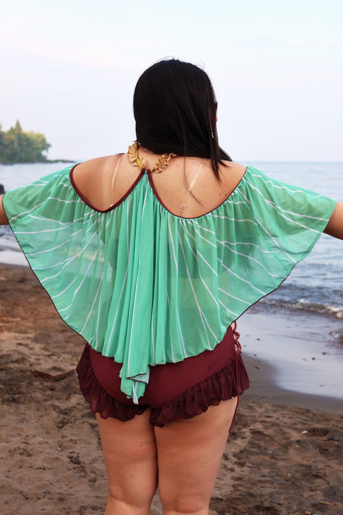Back view of the Nyahallo Luna Moth Swimsuit featuring a mint green moth wing-inspired cape with white wing detailing and burgundy ruffle bottoms.