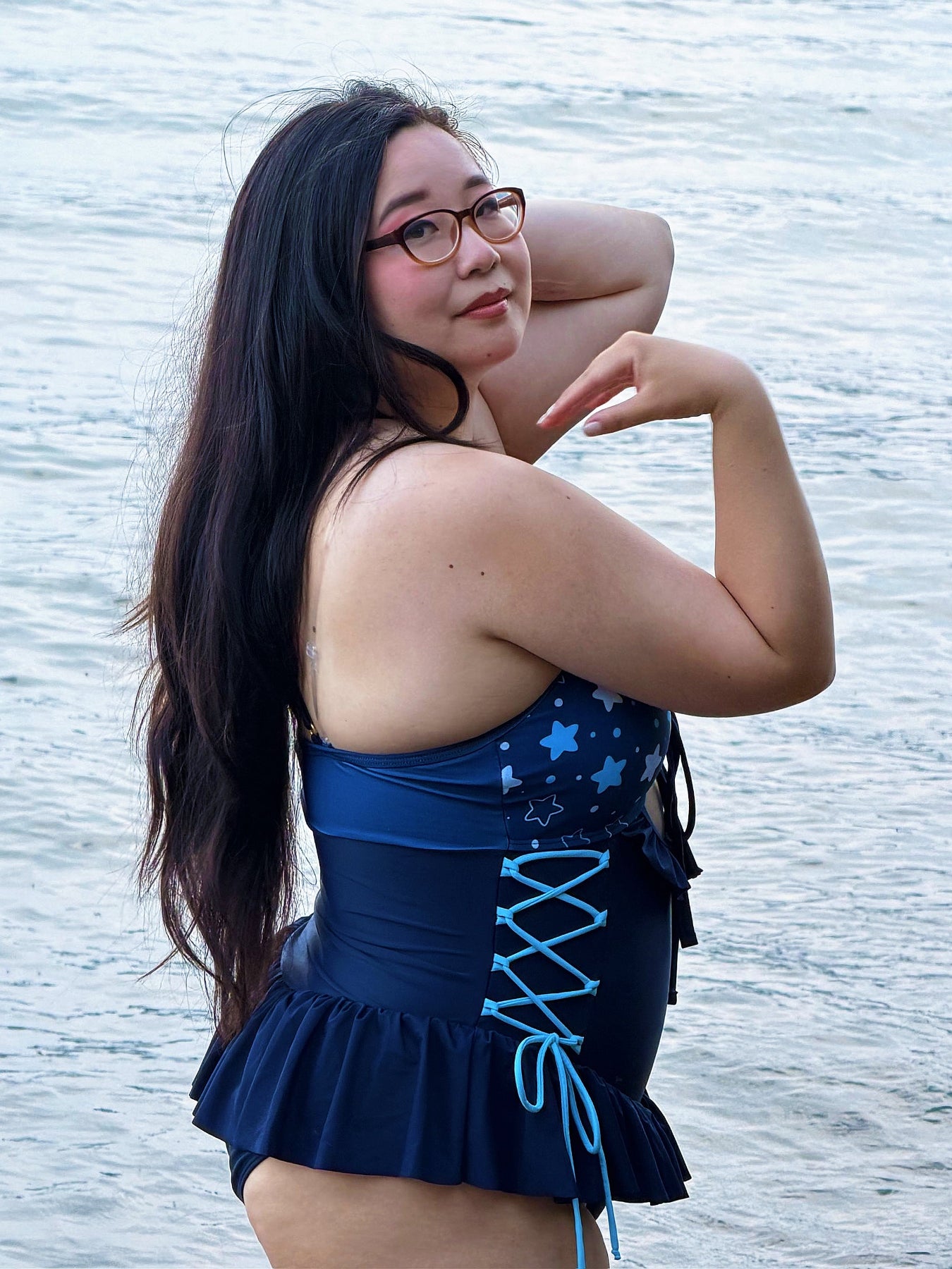 Side view of a model wearing the Nyahallo Moon Jellyfish Swimsuit without the detachable cape, featuring a navy one-piece with a star-patterned bust, lace-up sides, and ruffle skirt detail.