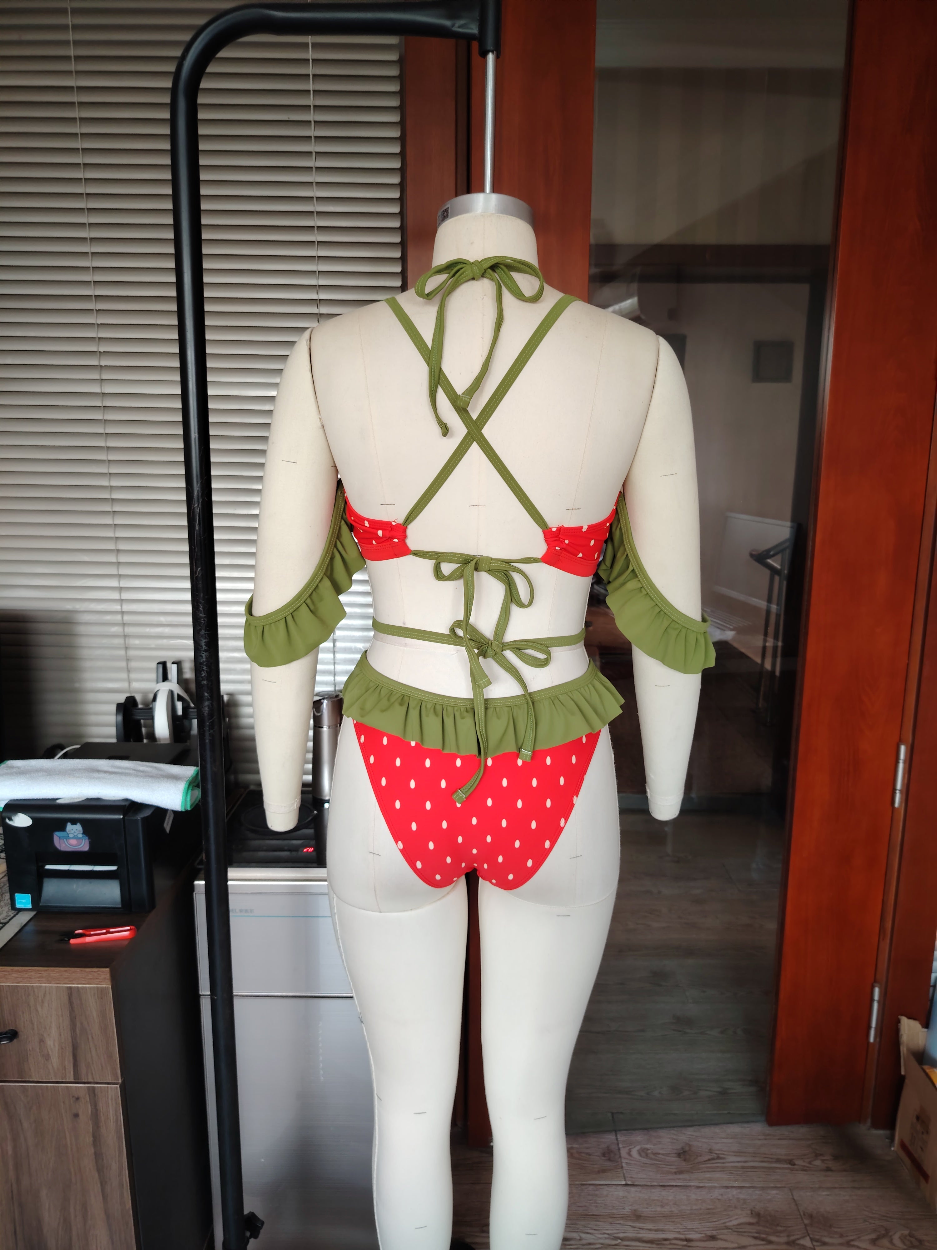 Mannequin wearing a red and green strawberry themed bikini in an indoor setting.