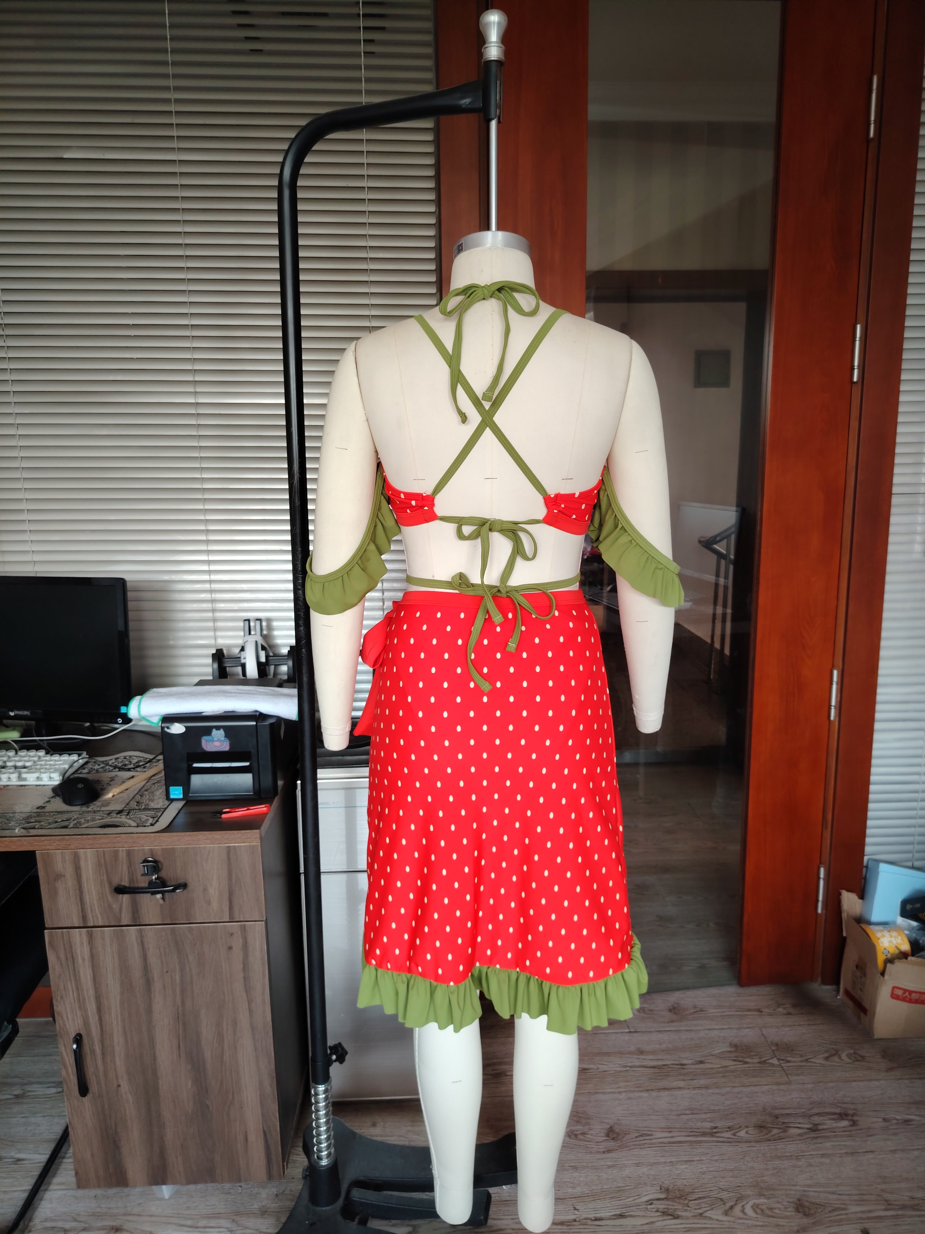 Mannequin wearing a red and green strawberry themed bikini with wrap skirt in an indoor setting.