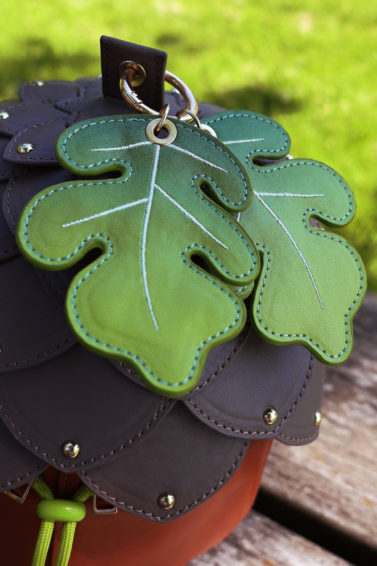 Close-up of embroidered oak leaf charms attached to an acorn-shaped crossbody bag with layered acorn cap details and gold hardware.