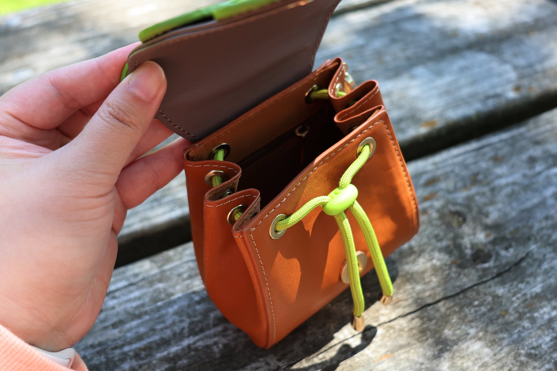 Top view of a small brown oak leaf pochette opened to display the drawstring closure and interior compartment, photographed outdoors on a wooden picnic table.