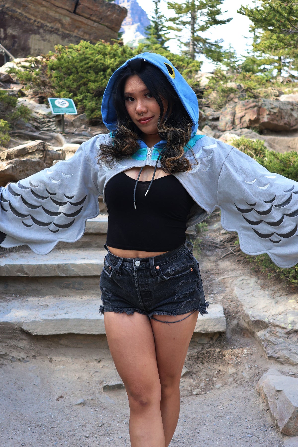 Close-up of the Nyahallo Pigeon Hoodie Shrug featuring a pigeon-inspired hood, embroidered feather details, and oversized wing-shaped sleeves spread open.