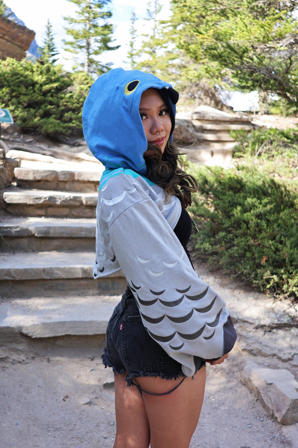 Side profile of the Pigeon Hoodie Shrug featuring a blue pigeon-inspired hood, embroidered feather sleeves, cropped oversized silhouette, and nature-inspired design.