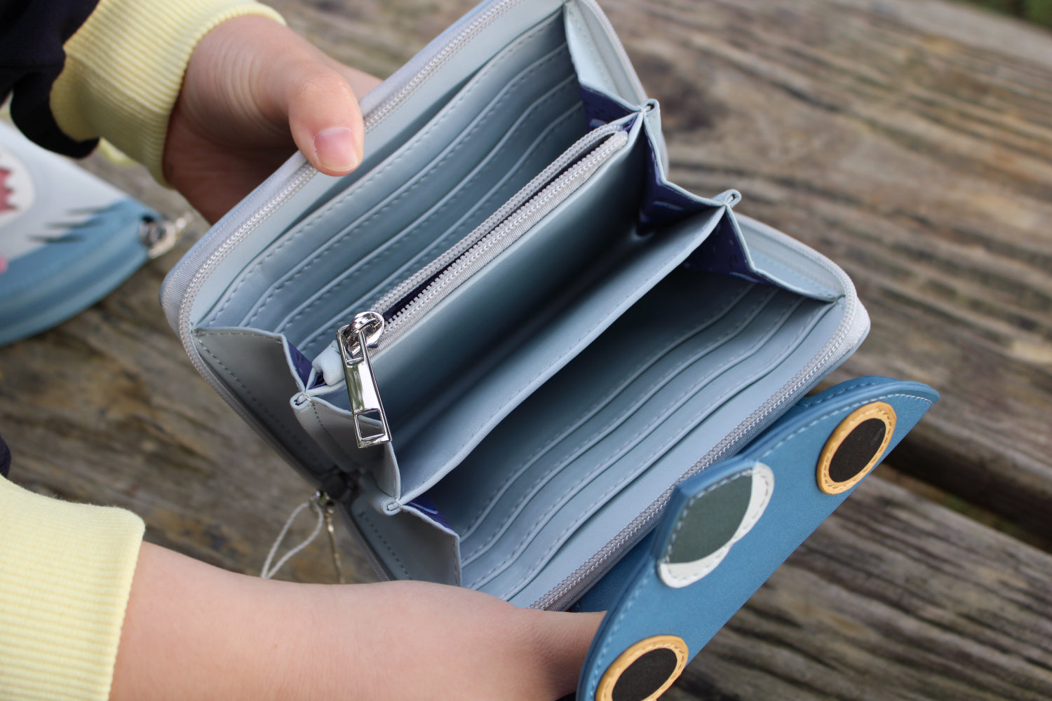 Open pigeon-shaped vegan leather wallet showing spacious card slots and zip coin compartment on a rustic wooden table.