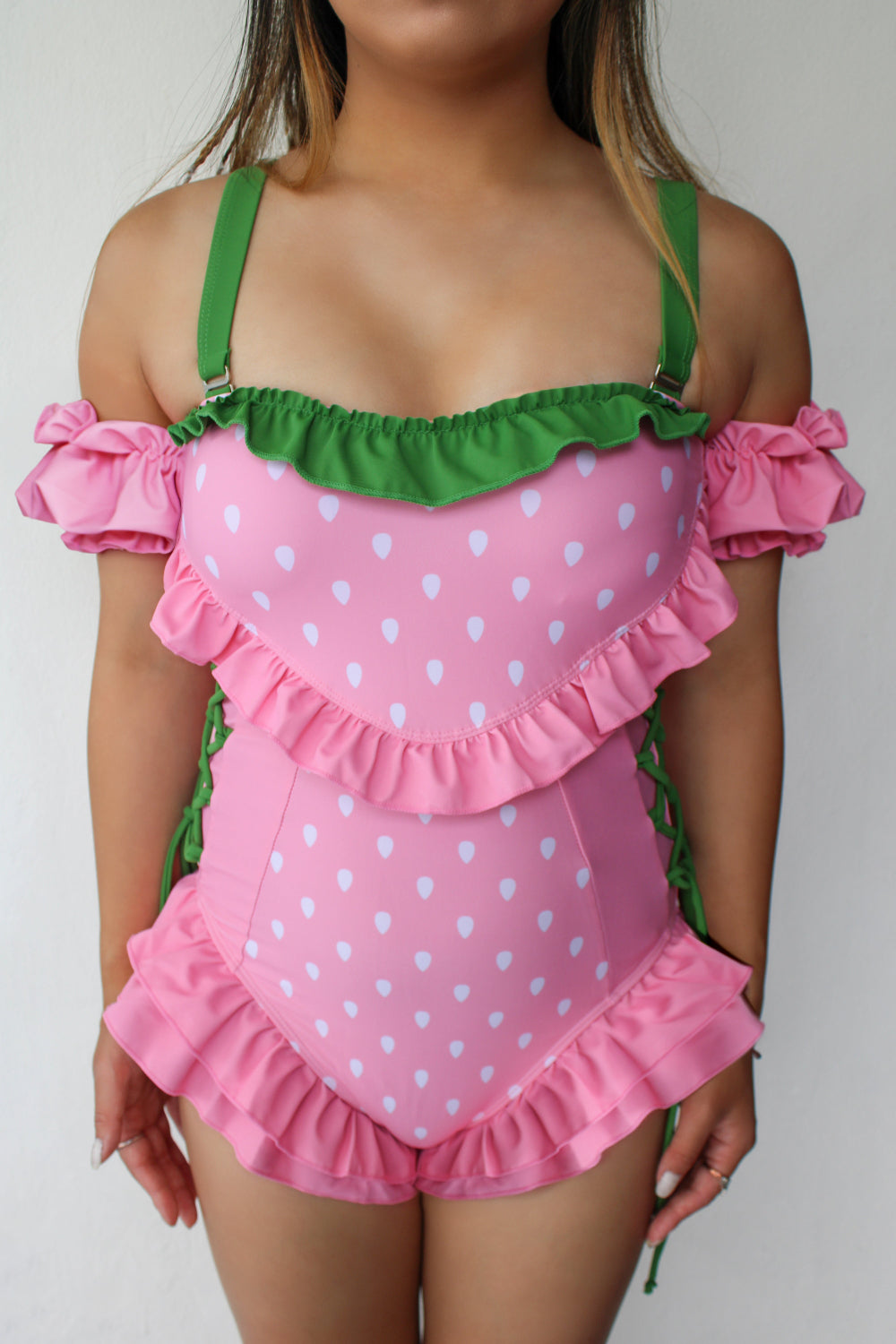 Pink strawberry-inspired swimsuit with puff sleeves, ruffle trim, side lace-up ties, and green accents in a whimsical fairycore style.