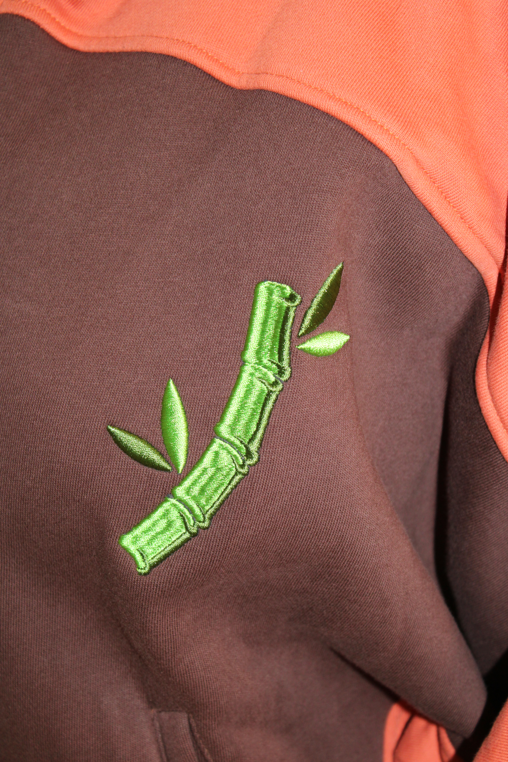 Close-up of green bamboo embroidery on a brown and orange red panda hoodie.
