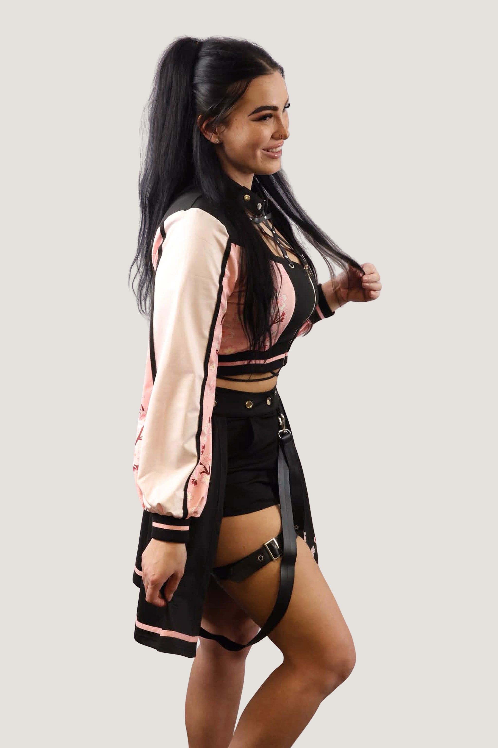 Model wearing a black and pink outfit with a harness on a plain background