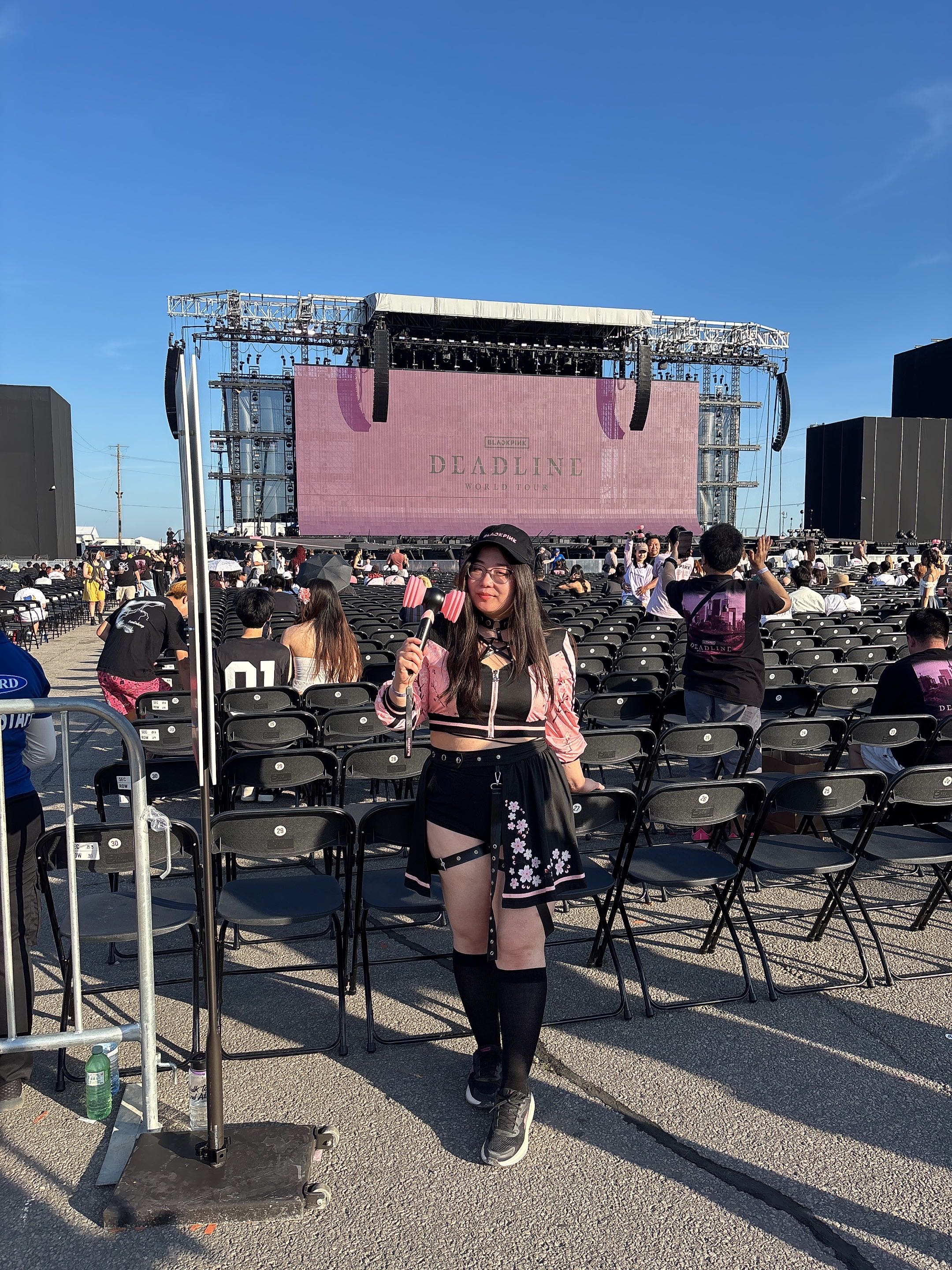 A model wearing the Sakura floral superstar set at a BLACKPINK concert, holding a lightstick in front of the 'Deadline World Tour' stage.
