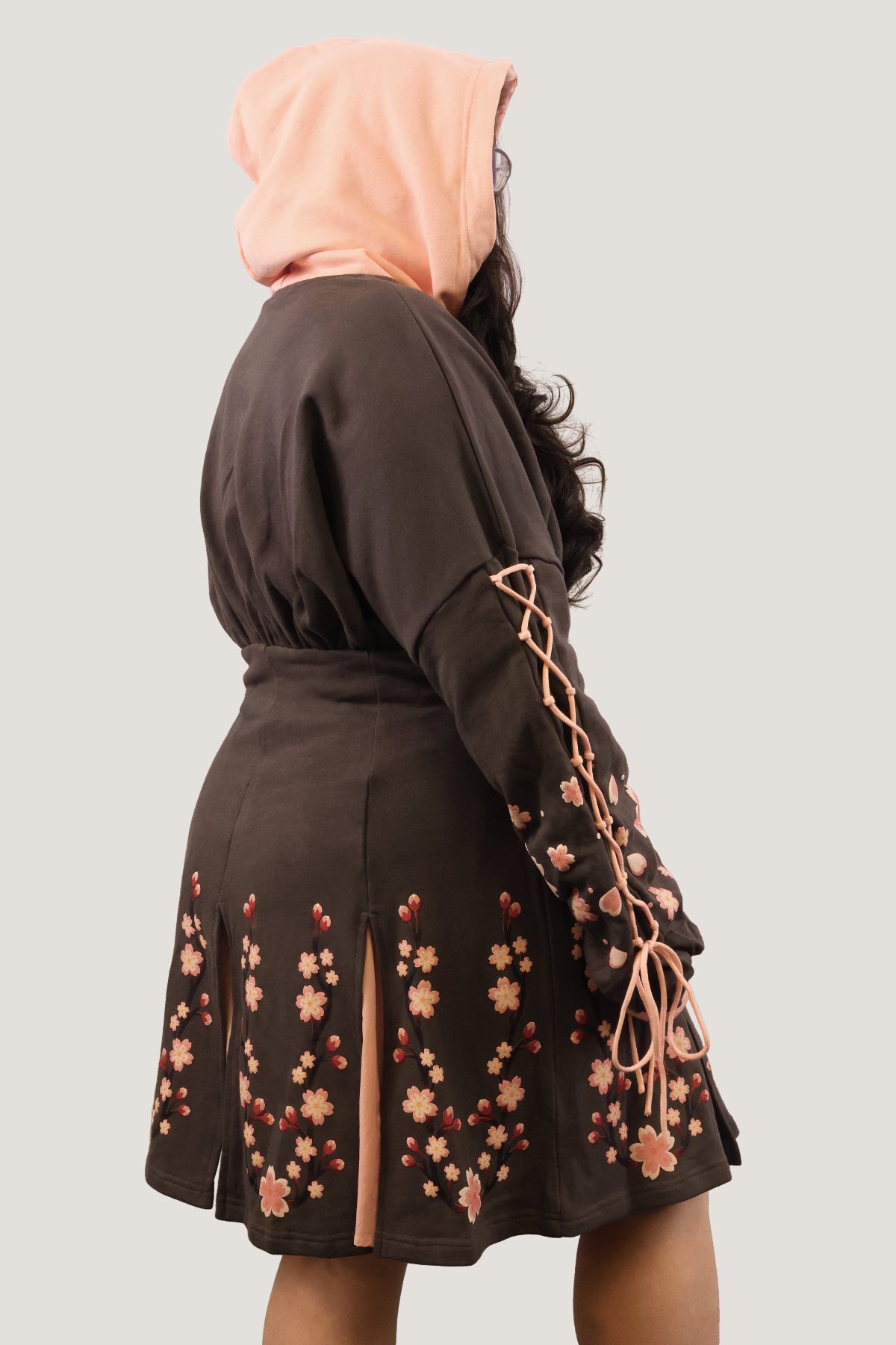 Side back view of the Sakura Hoodie Dress with cherry blossom details, lace-up sleeves, and a pink hood.