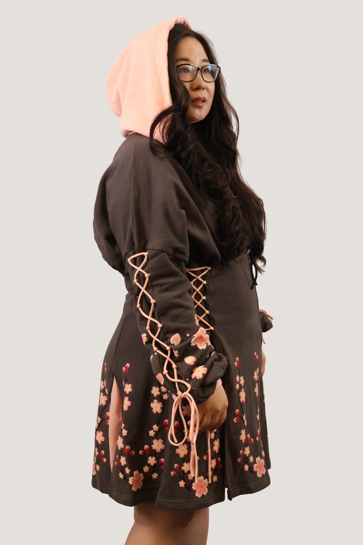 Side profile of the Sakura Hoodie Dress with the hood up, featuring lace-up sleeves and cherry blossom details.