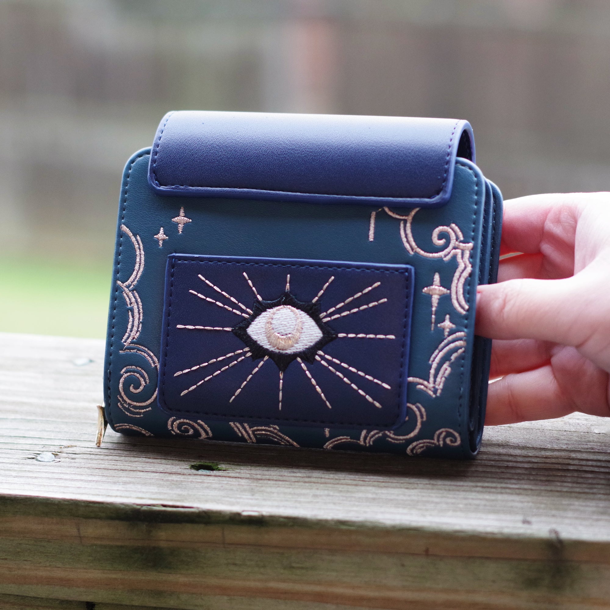 Back view of the Seraphim angel wallet featuring embroidered celestial eye artwork, gold star detailing, and deep blue vegan leather.