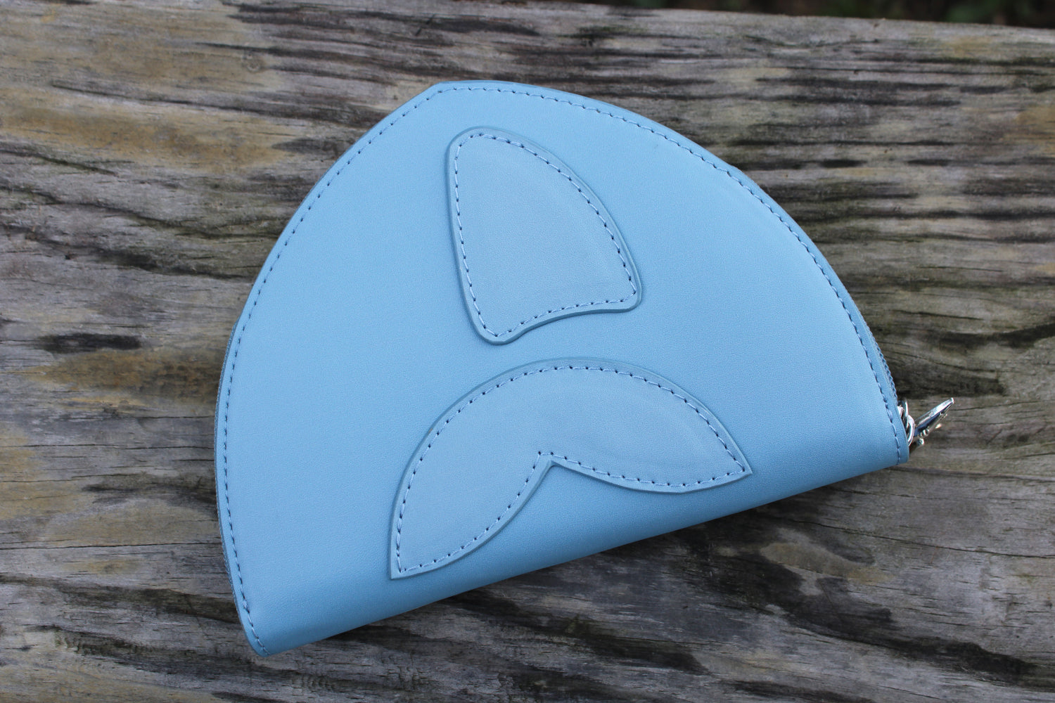 Back view of a cute shark-shaped vegan leather wallet featuring stitched fin and tail details on a soft blue design.