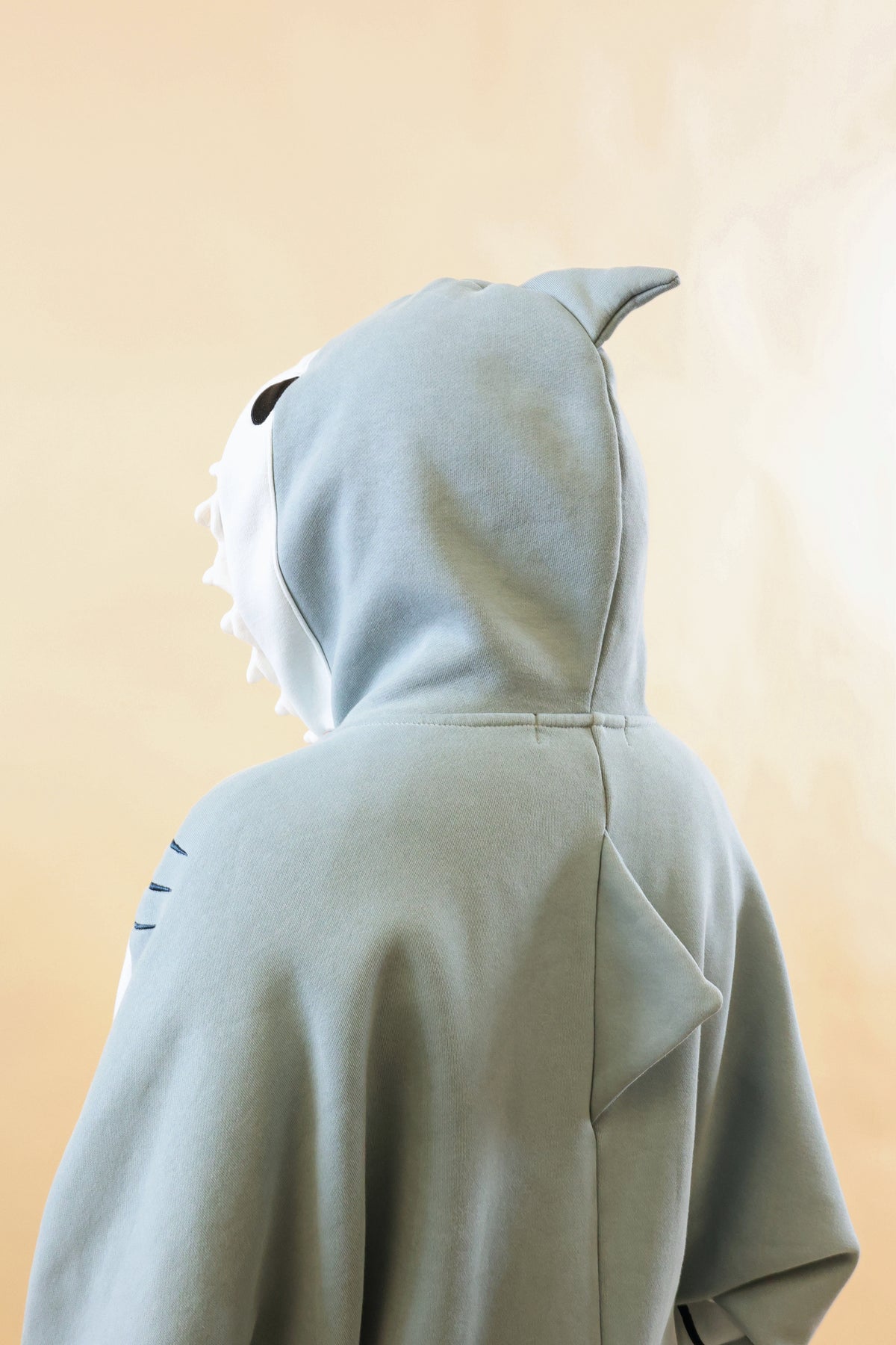 Close-up back view of the Nyahallo Shark Hoodie, highlighting its light blue shark hood with dorsal fin, white teeth detailing, embroidered gills, and triangular back fin.