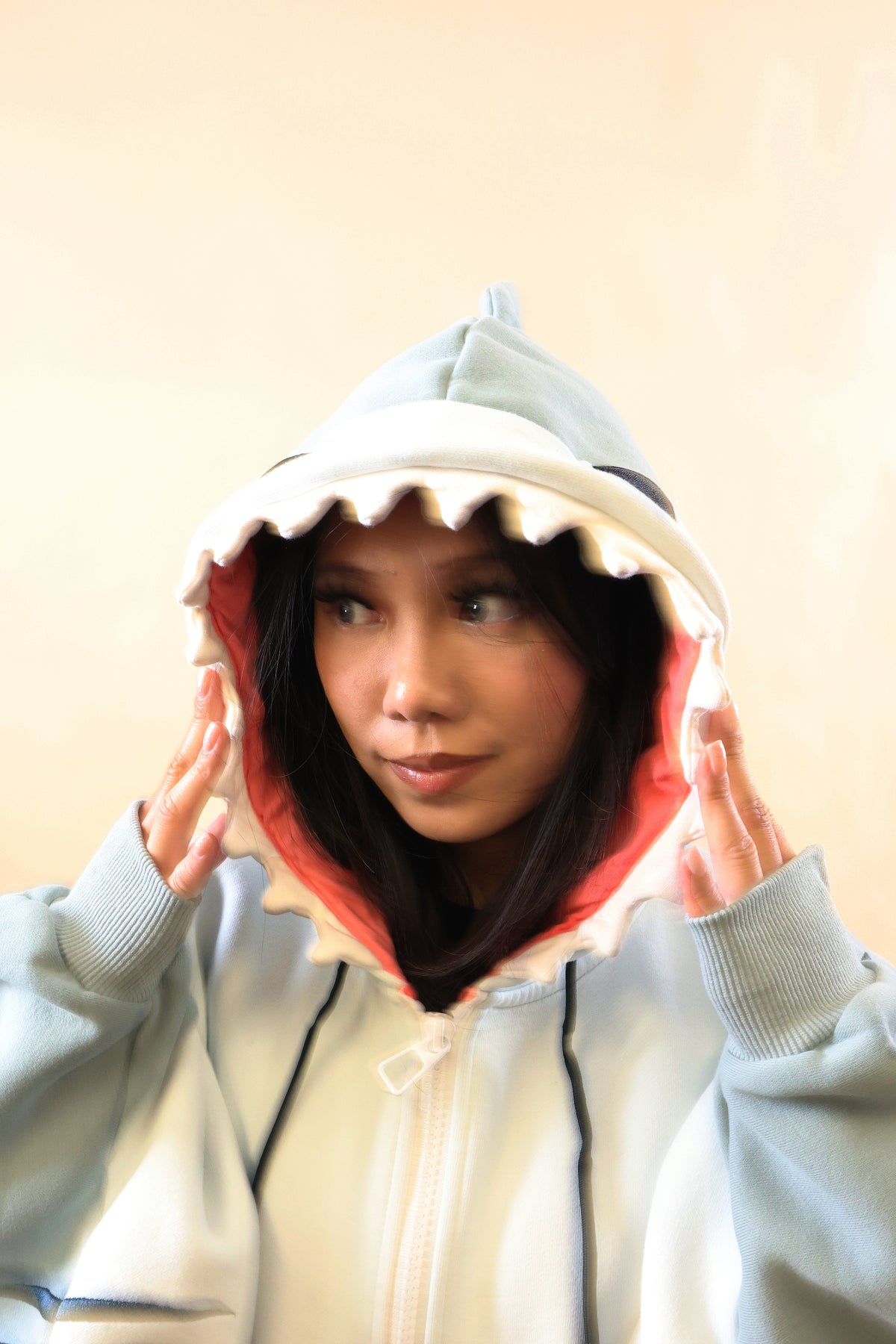Close-up of a model wearing the Nyahallo Shark Hoodie, highlighting its light blue shark hood with white teeth, pink lining, dorsal fin, and oversized sleeves.