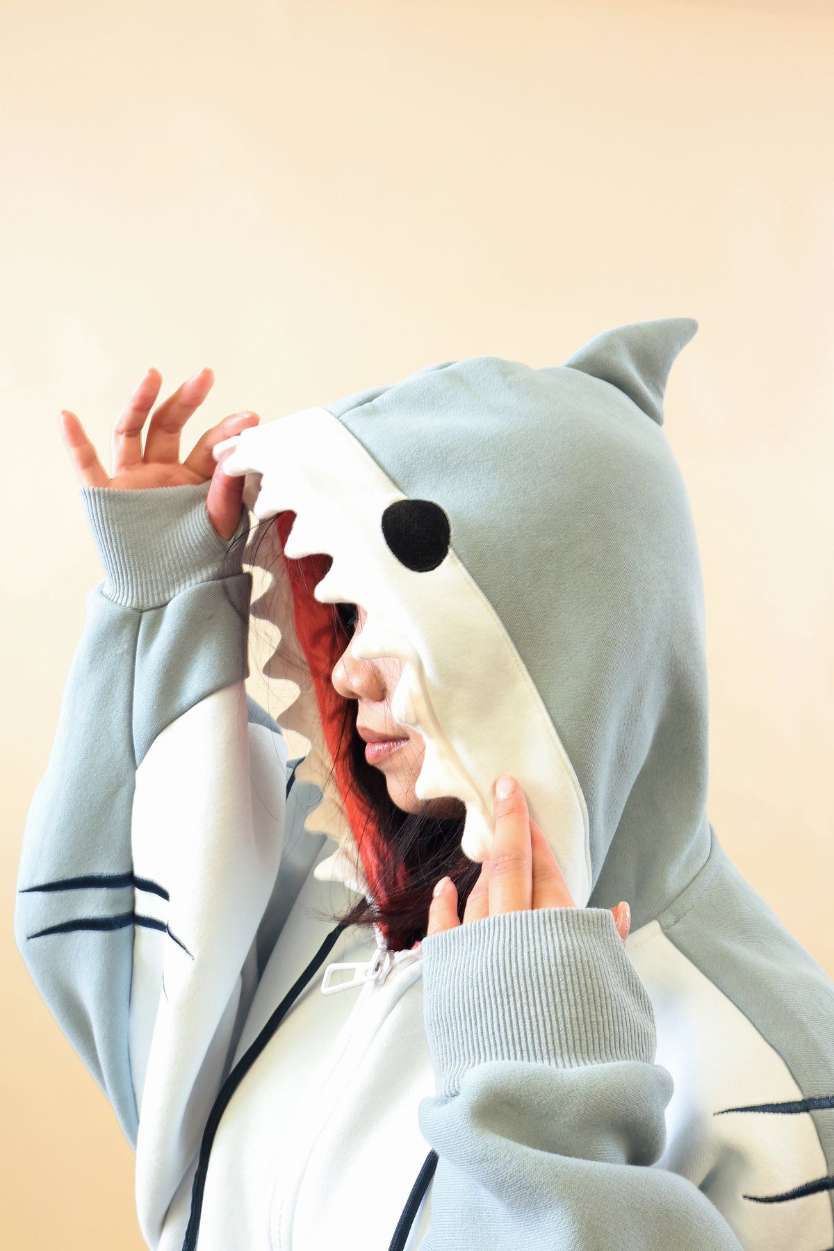 Close-up side view of the Nyahallo Shark Hoodie, highlighting its light blue shark hood with dorsal fin, black eye, white teeth, pink lining, and embroidered gill details.