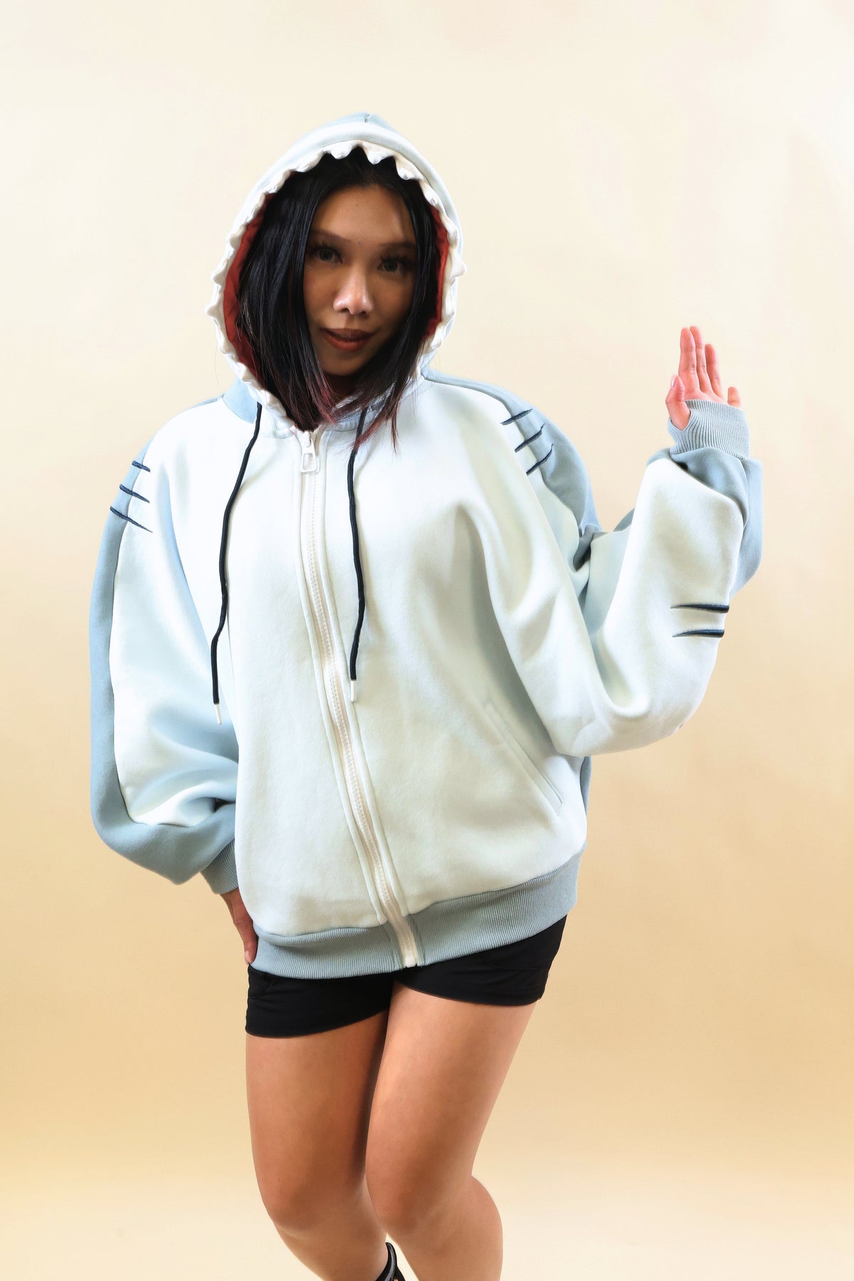 Front view of a model wearing the Nyahallo Shark Hoodie, featuring a light blue and white zip-up design, shark teeth hood, embroidered gill details, oversized sleeves, and front pockets.