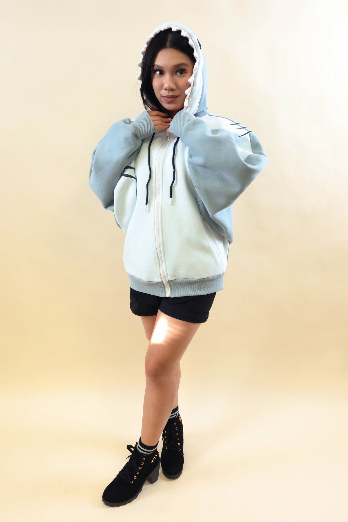 Full-body front view of a model wearing the Nyahallo Shark Hoodie, featuring a light blue and white zip-up design, shark teeth hood, oversized sleeves, embroidered gill details, and front pockets.