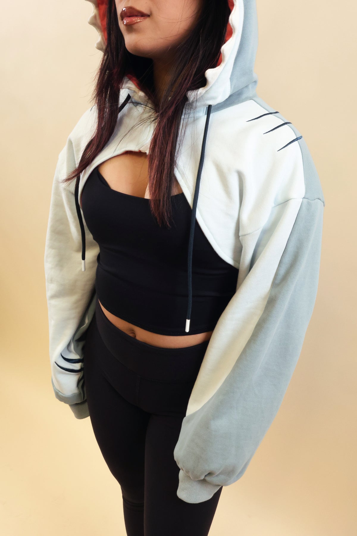 Close-up of the Nyahallo Shark Shrug, highlighting its light blue and white cropped design, oversized sleeves, embroidered gill details, and adjustable hood drawstrings.