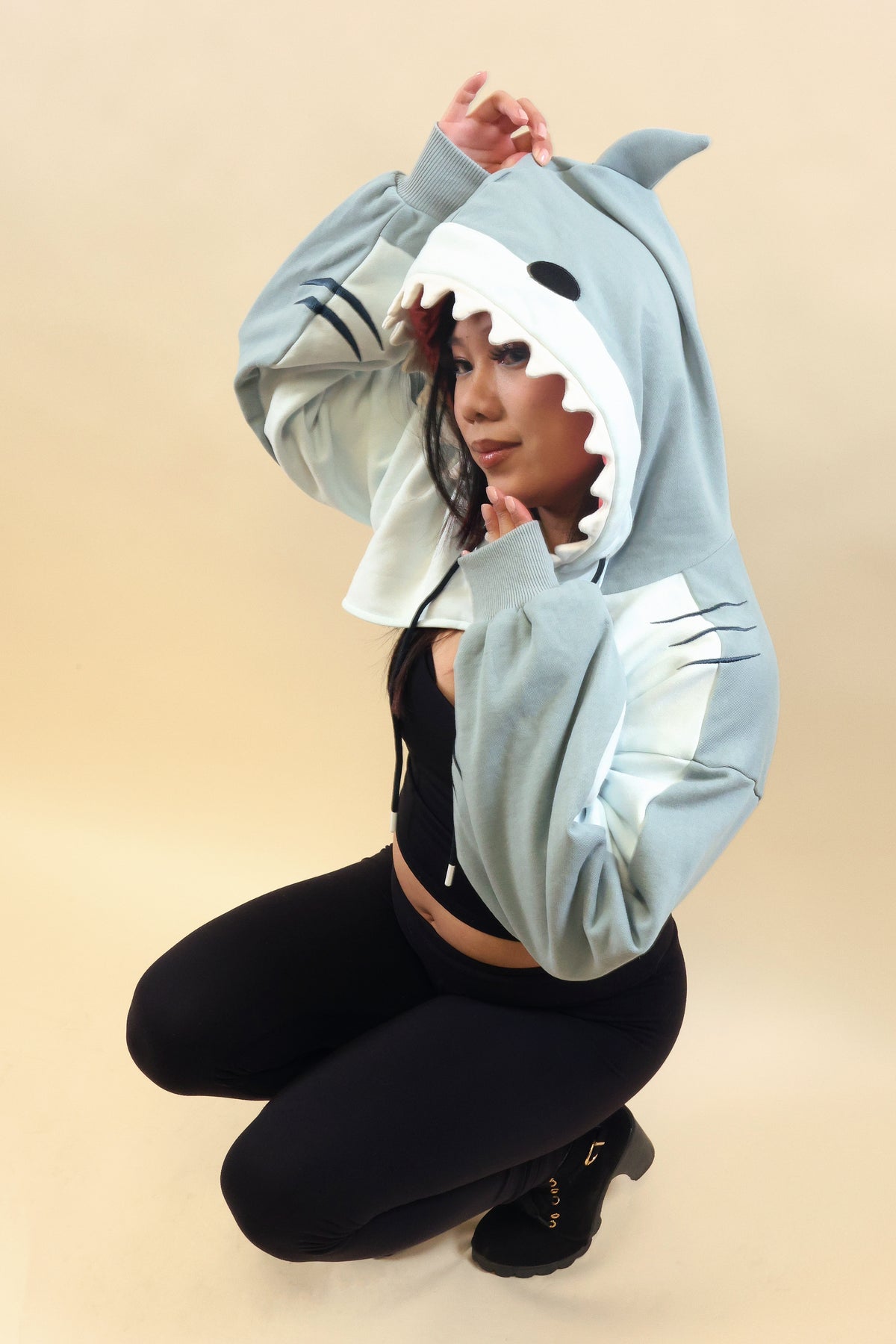 Side view of a model wearing the Nyahallo Shark Shrug, featuring a light blue shark hood with white teeth, dorsal fin, embroidered gill details, and oversized sleeves.