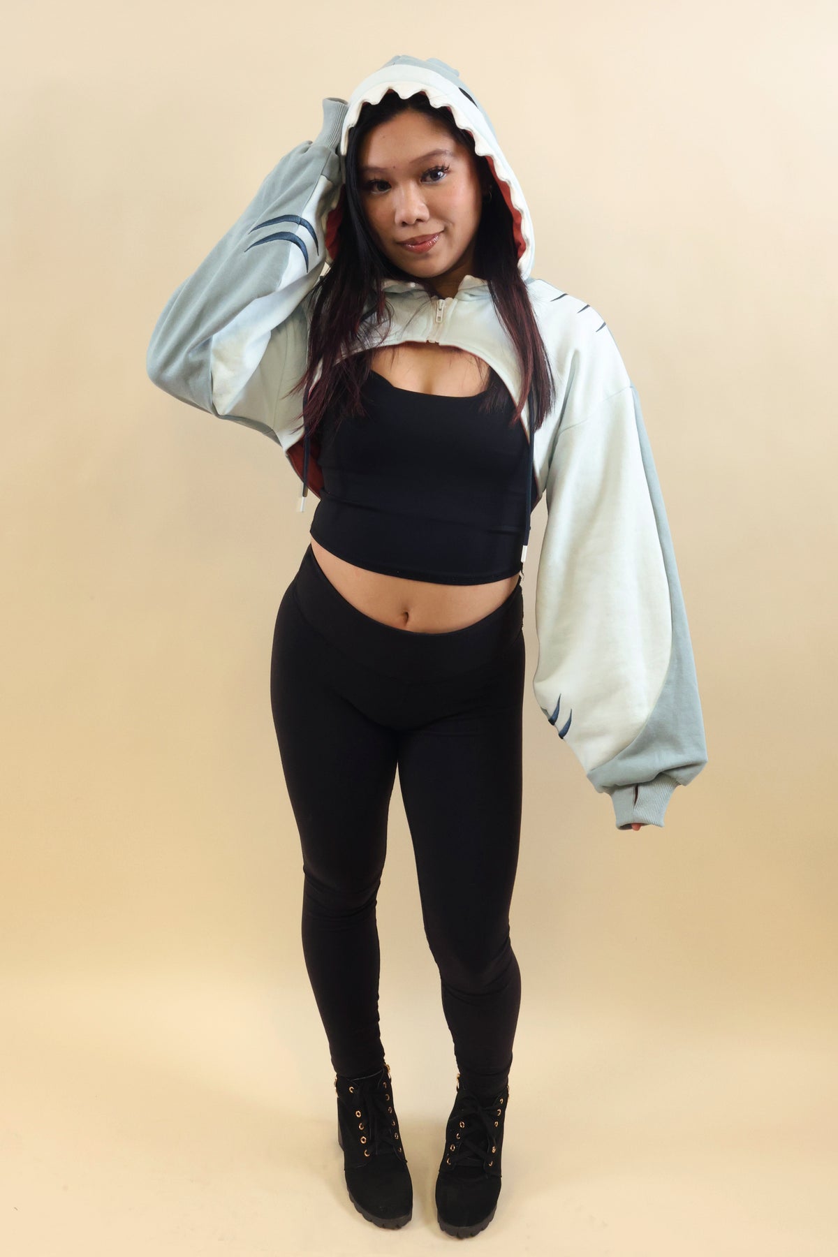 Full-body front view of a model wearing the Nyahallo Shark Shrug, featuring a light blue shark hood with white teeth, oversized sleeves, and a cropped design over a black outfit.