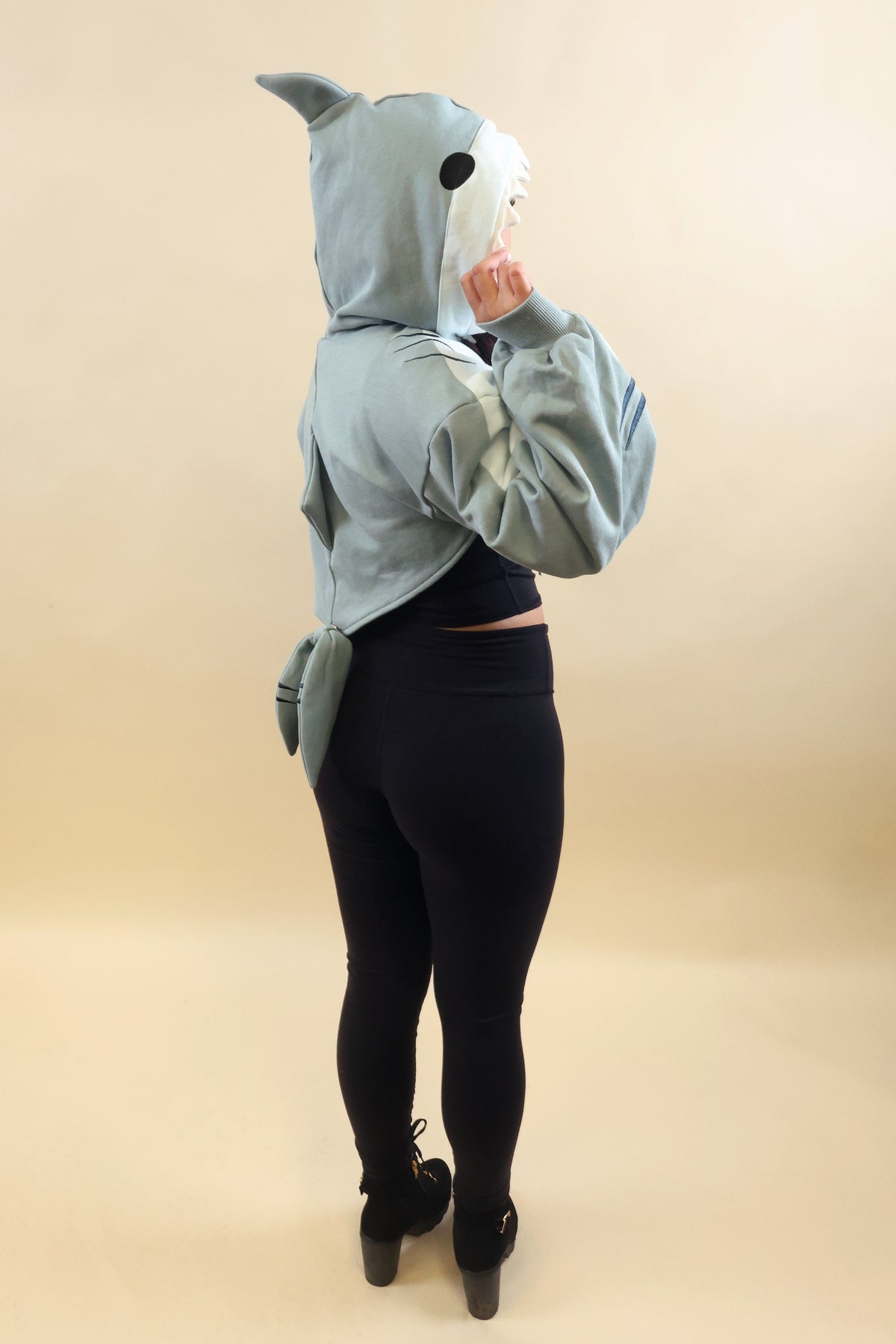 Side and back view of a model wearing the Nyahallo Shark Shrug, featuring a light blue shark hood with dorsal fin, oversized sleeves, back fin, and dangling shark tail.