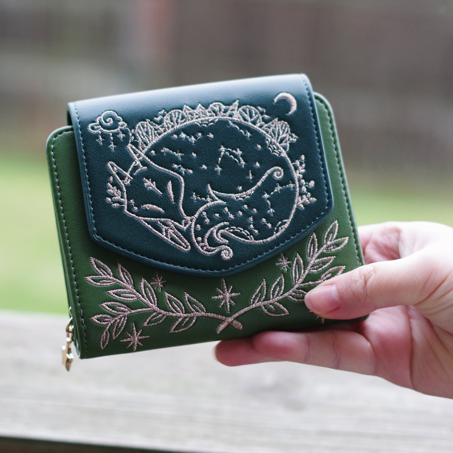 Green Slumbering Forest fantasy wallet with embroidered sleeping fox design, moon details, and botanical accents held in hand.