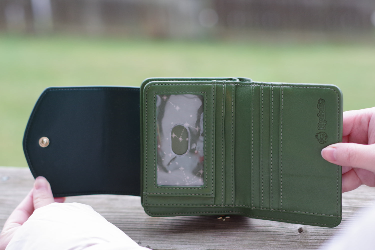 Open green fantasy wallet with multiple card slots, ID window, and celestial forest-themed lining held outdoors.