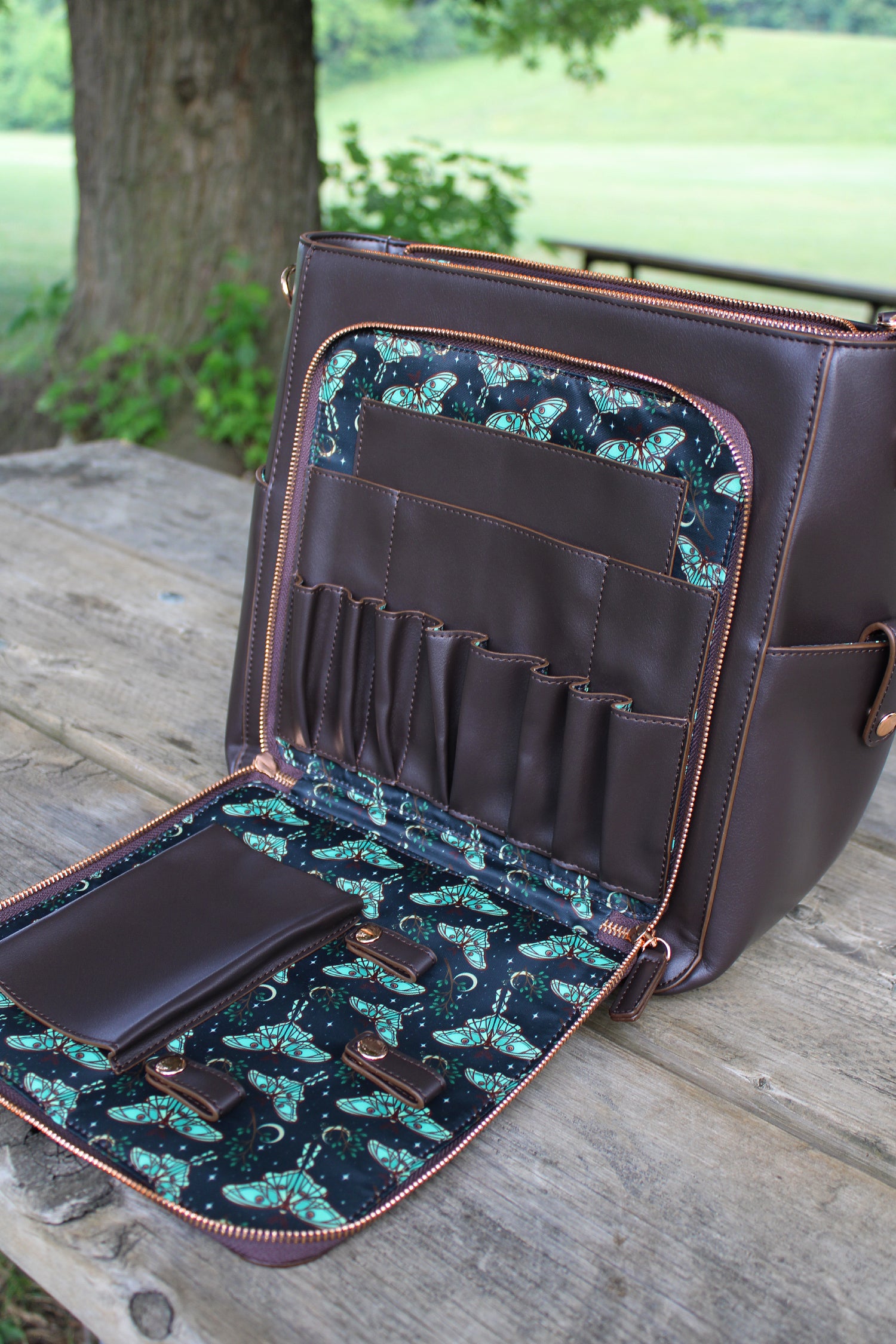 Spanish moon moth backpack opened to show organizer compartments and printed moth lining on a wooden table outdoors.