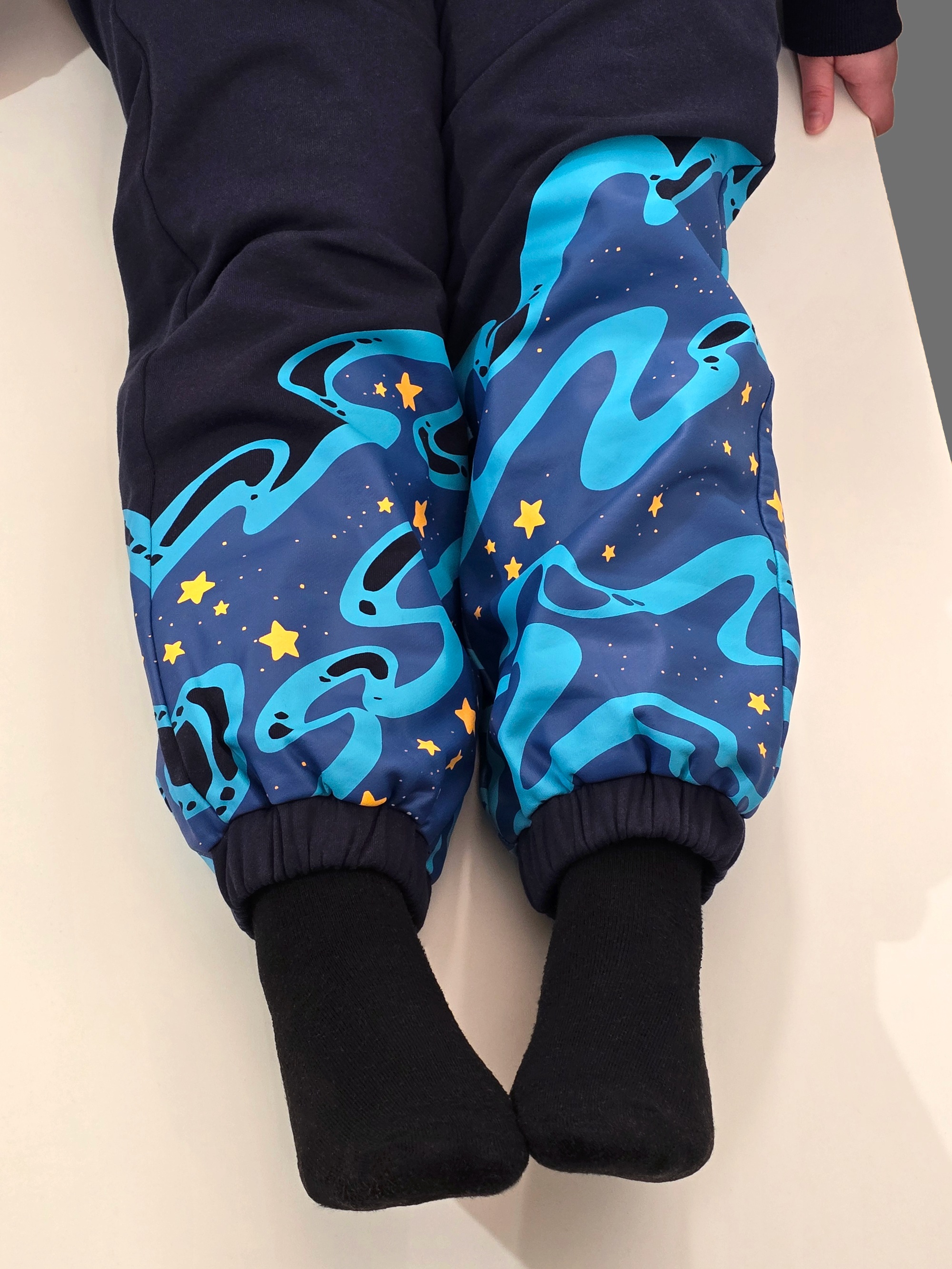 Close-up of navy Stellar Tide sweatpants featuring blue celestial wave patterns and yellow star prints near the cuffed ankles.