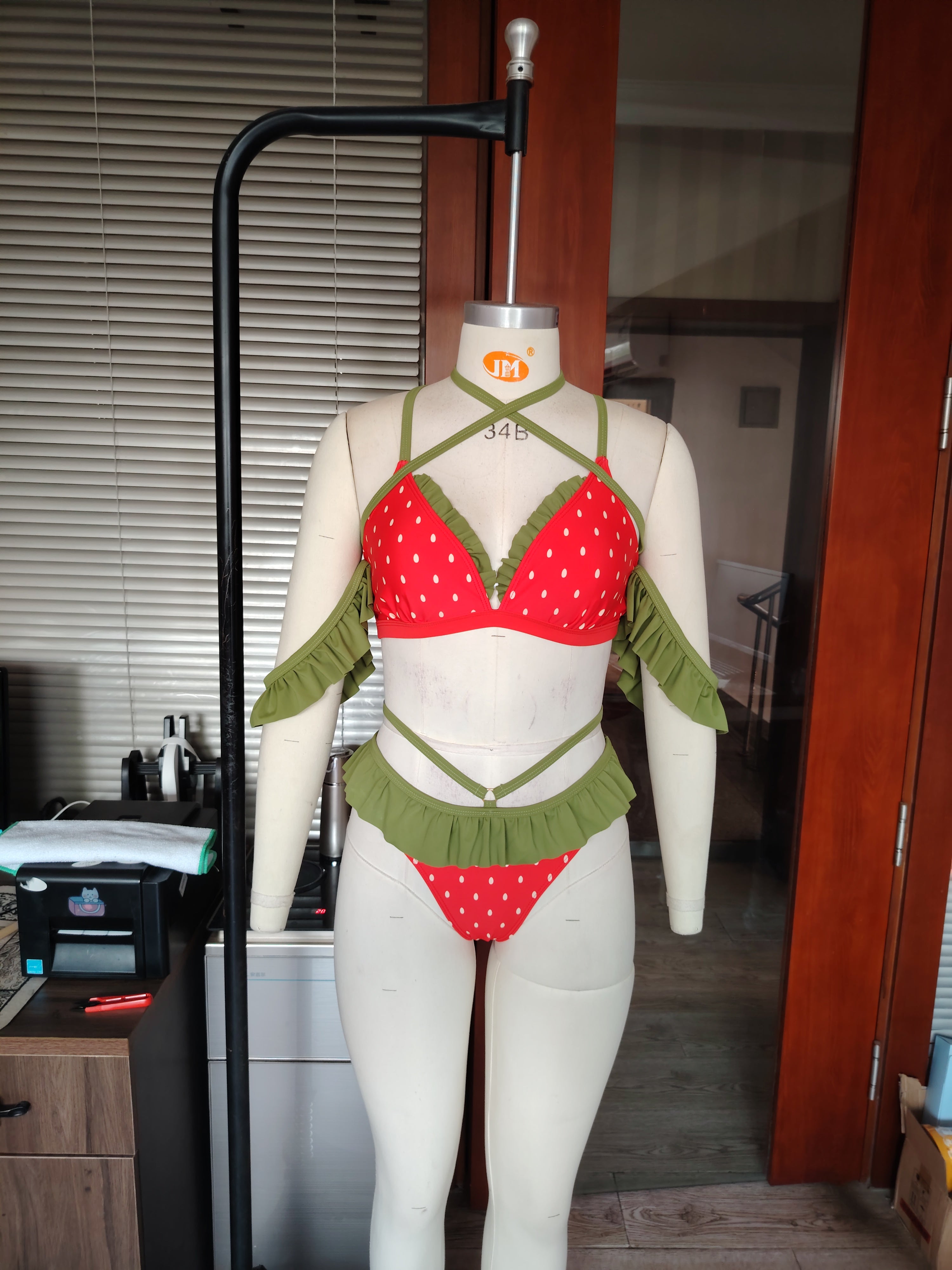 Mannequin wearing a red and green strawberry themed bikini in an indoor setting.