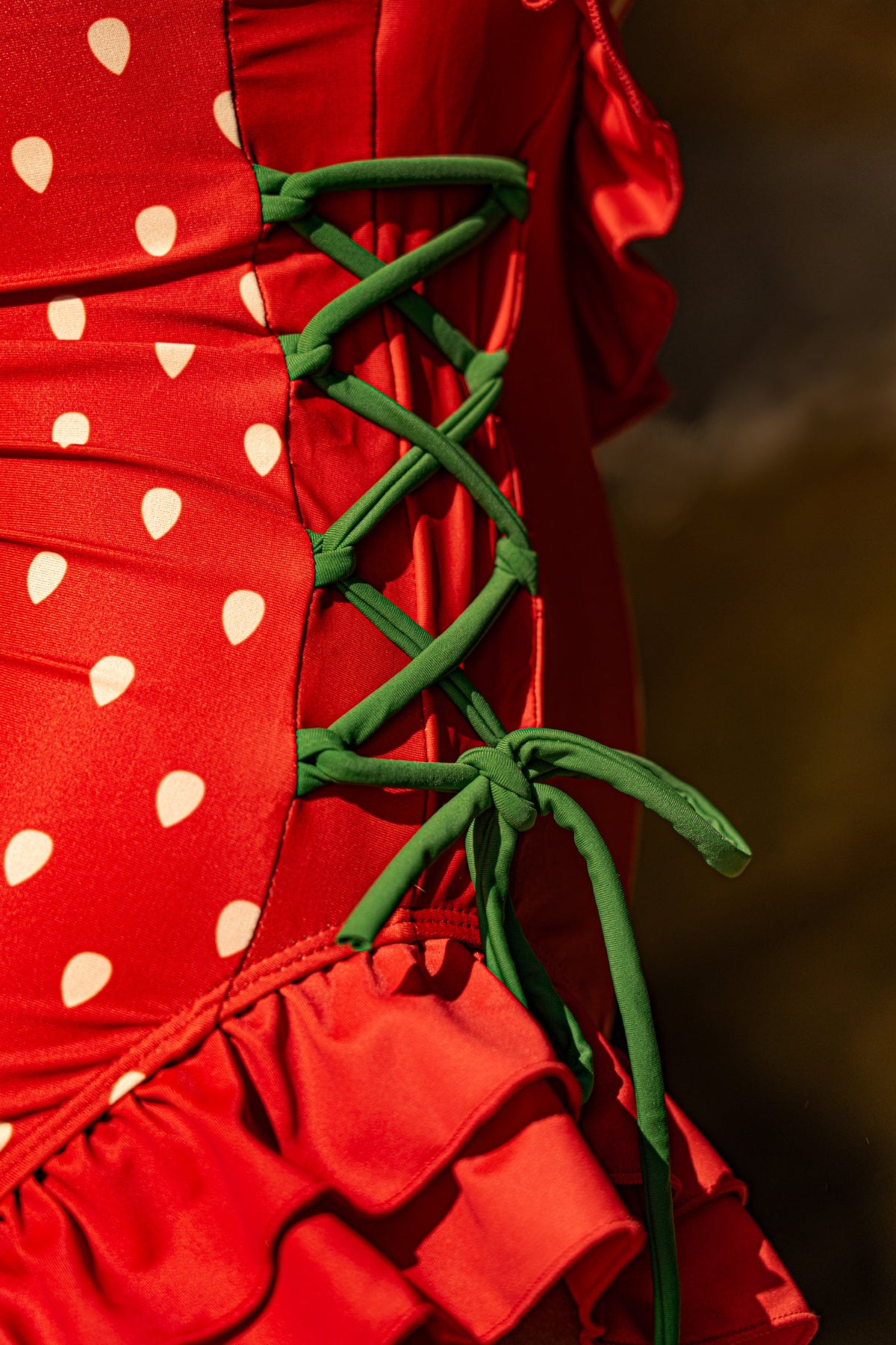 Close-up of the adjustable green side lace-up ties on the Nyahallo Strawberry One-Piece Swimsuit, featuring a strawberry print, ruffle hem, and customizable fit.