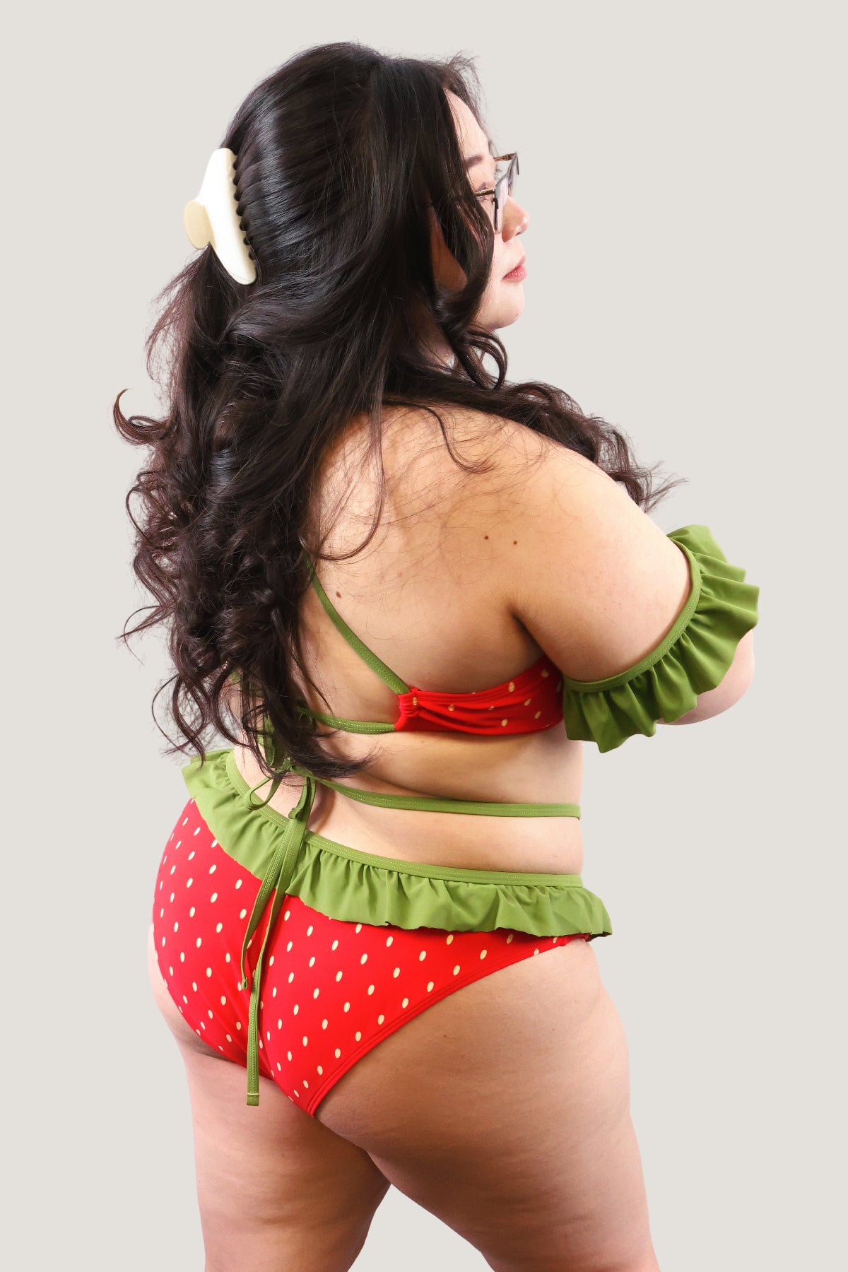 Model wearing a red and green strawberry-themed swimsuit on a plain background