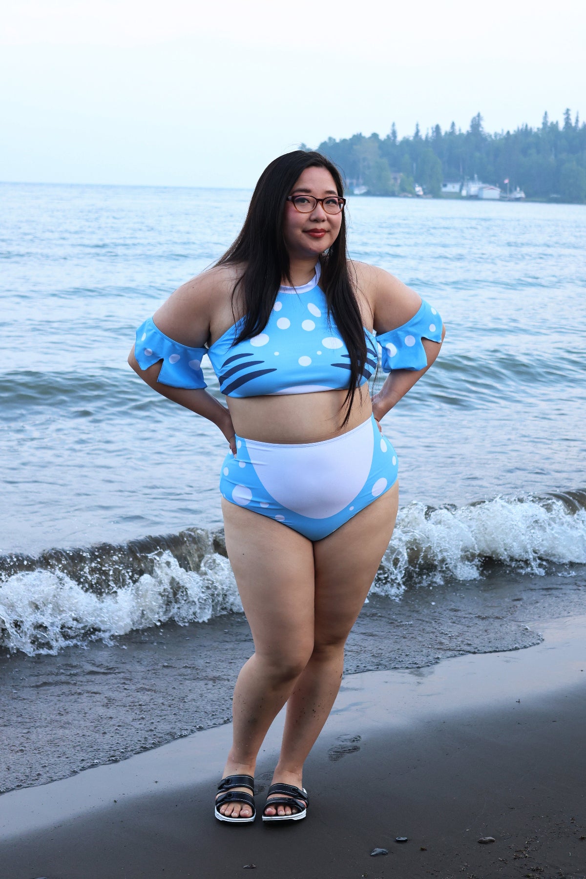 Full-body front view of the blue and white Whale Shark two-piece swimsuit with spotted details and fin-inspired sleeves, photographed by the water.