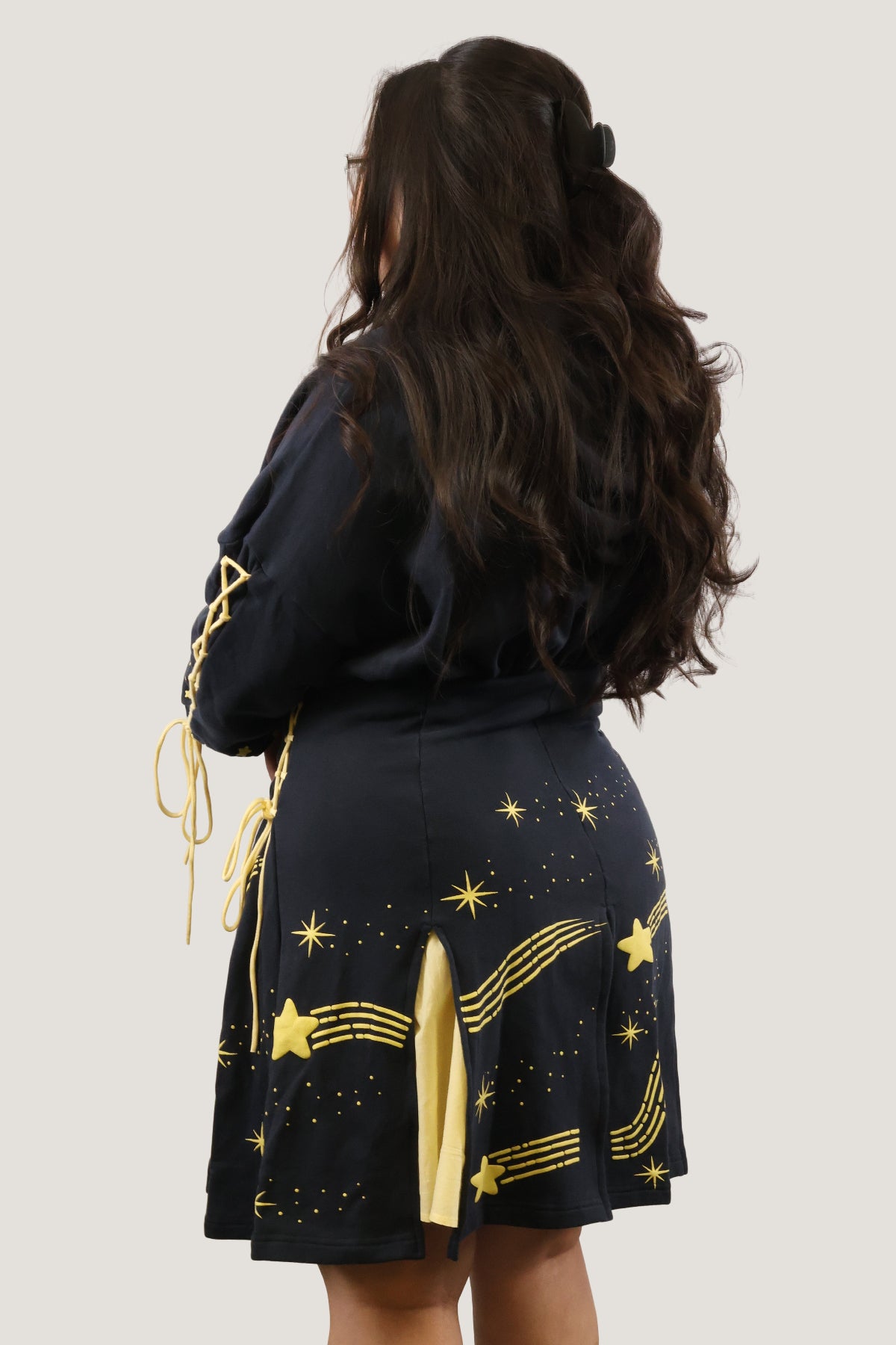 Back view of the Wish Upon a Star Hoodie Dress showcasing the gold star and shooting star print, lace-up sleeve details, and layered yellow skirt panels.