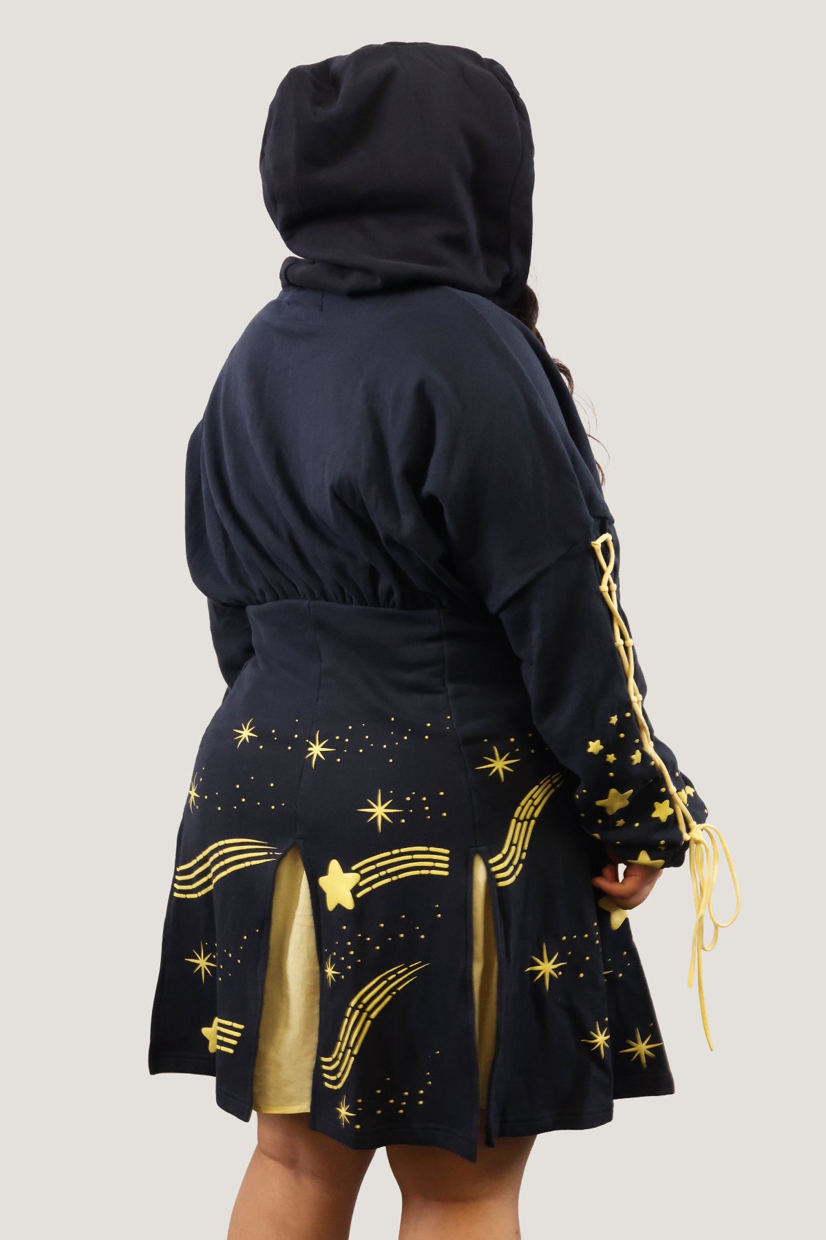 Back view of the Wish Upon a Star Hoodie Dress with hood up, featuring gold puff print stars, lace-up sleeves, and layered yellow skirt panels.