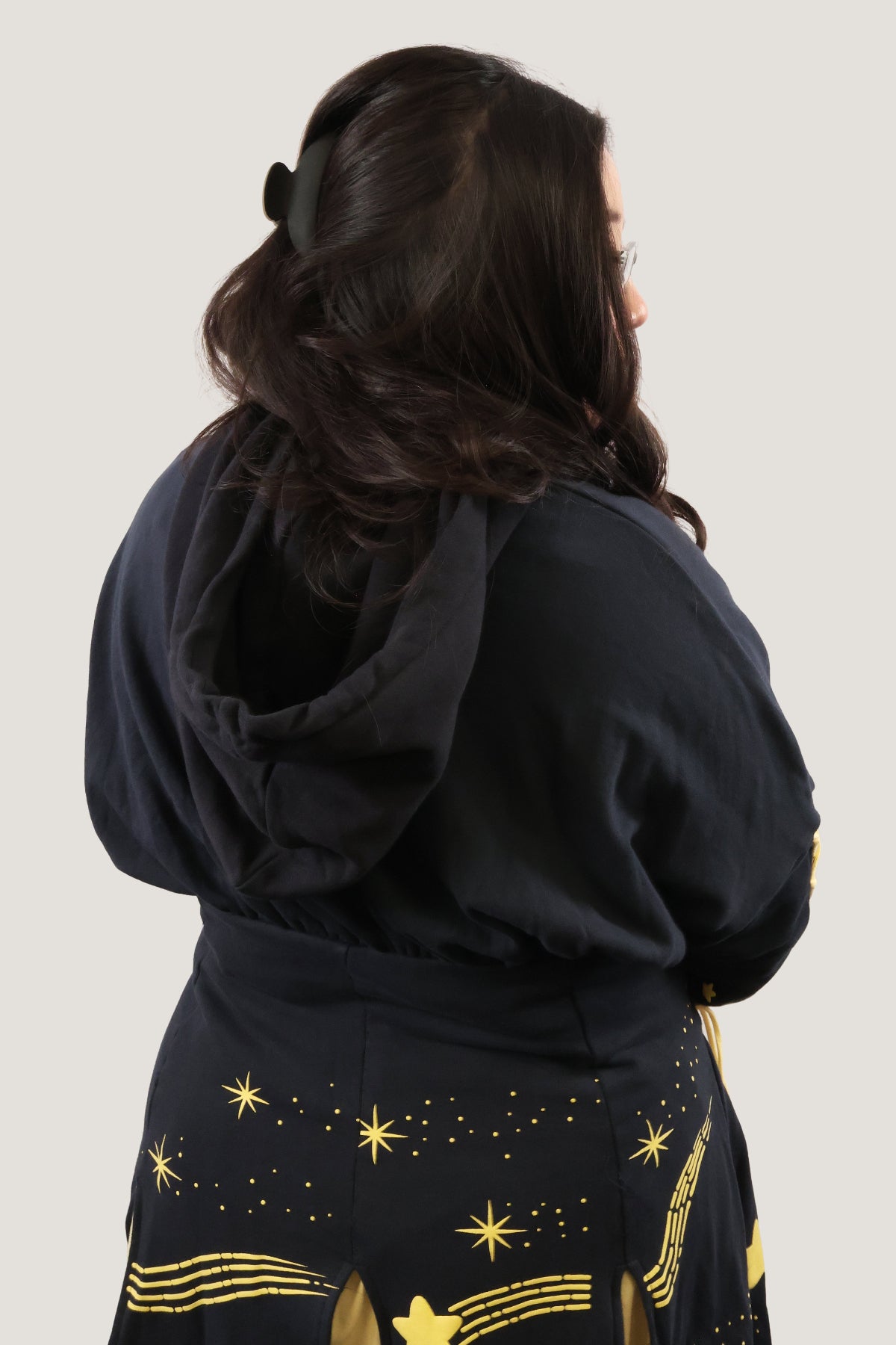 Back view of a model wearing the Wish Upon a Star Hoodie Dress, featuring a roomy hood and whimsical gold celestial print on a navy hoodie dress.