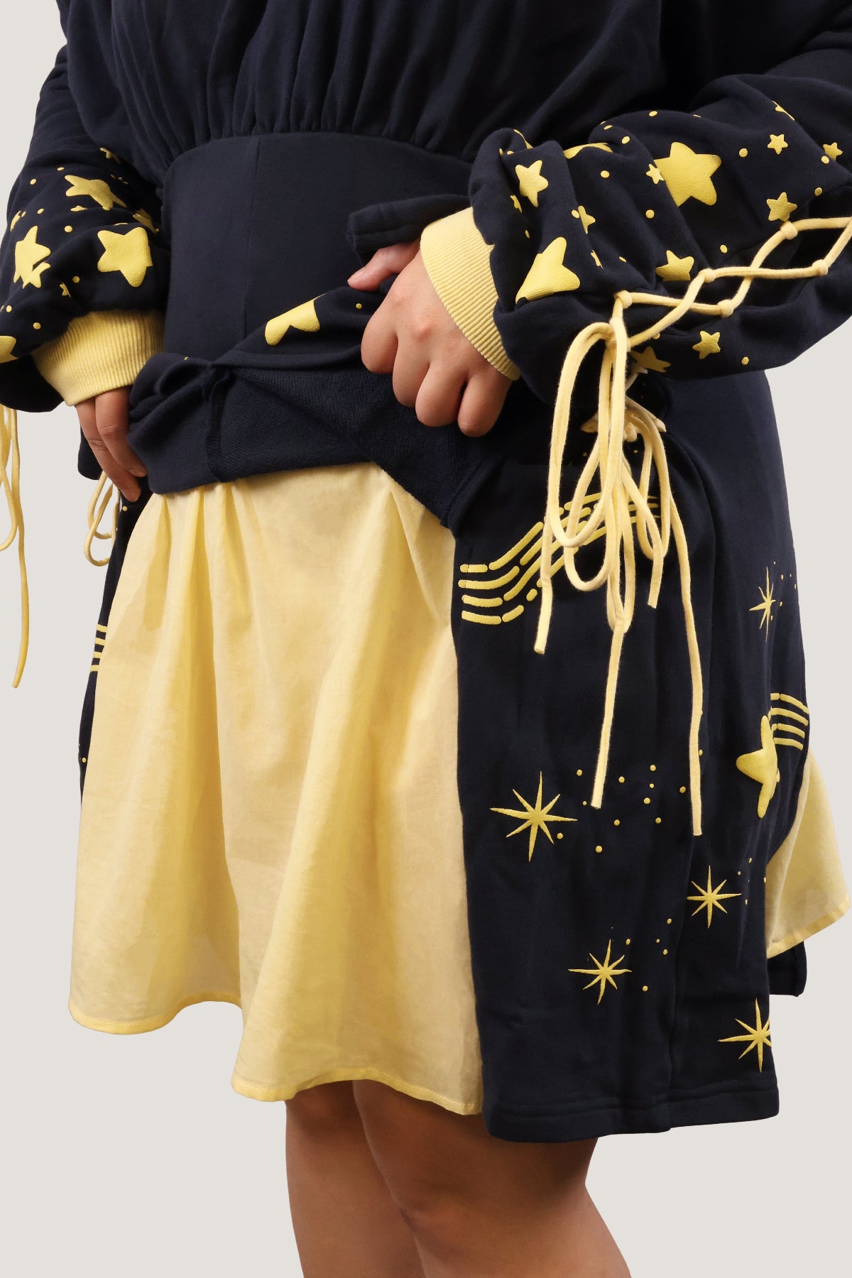 Close-up of the Wish Upon a Star Hoodie Dress showing the lace-up sleeves, puff print stars, and layered yellow skirt detail.