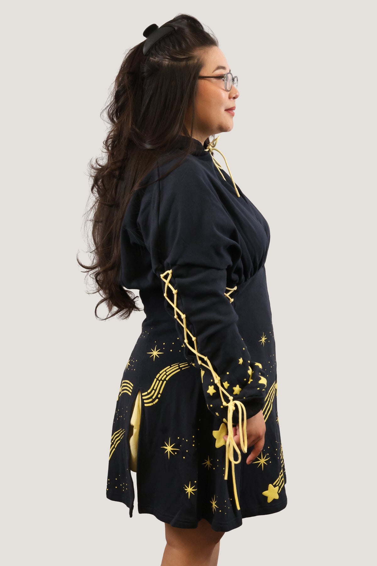 Side view of a model wearing the Wish Upon a Star Hoodie Dress, showcasing lace-up sleeve details and gold celestial print on a whimsical navy hoodie dress.