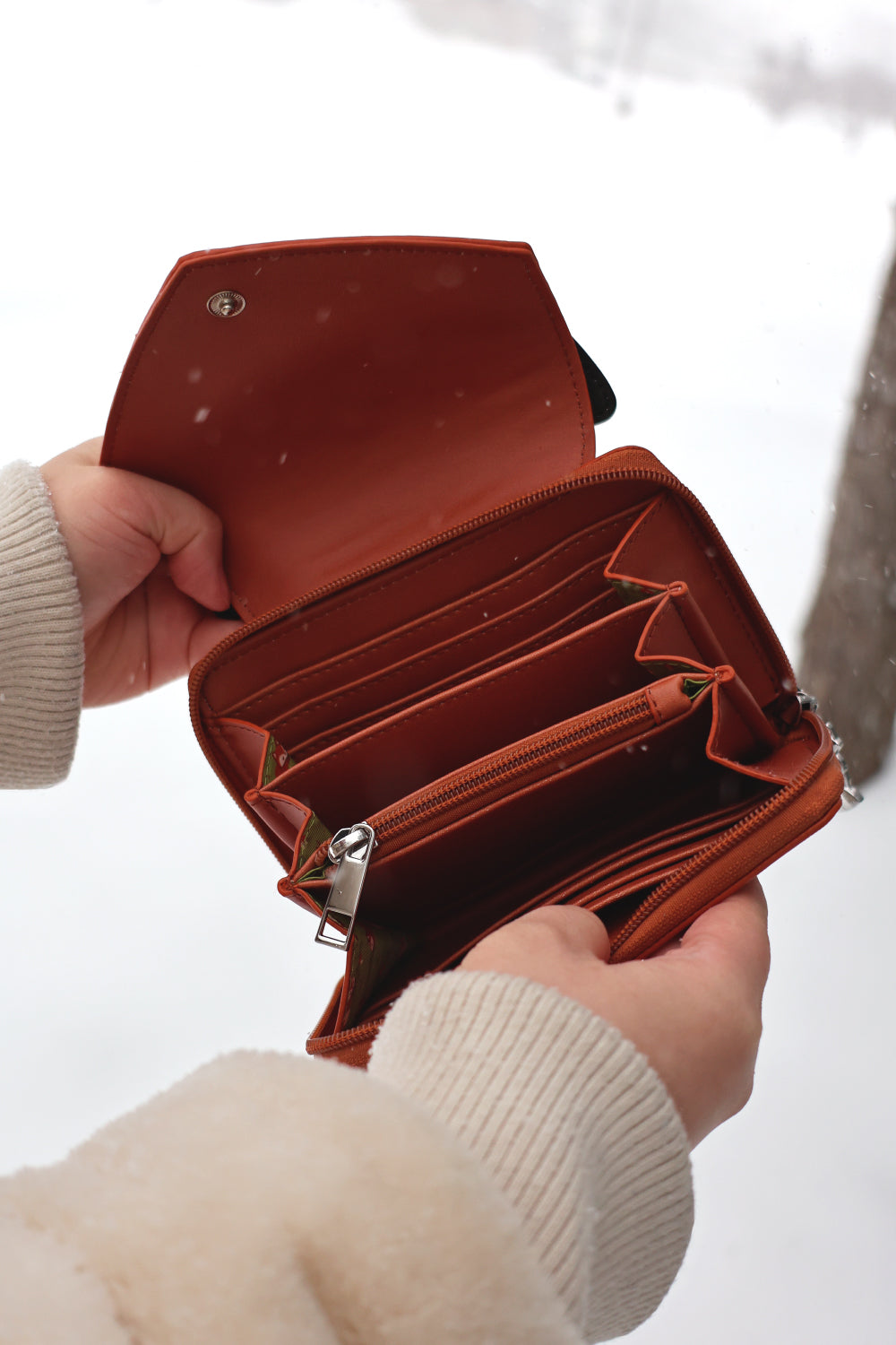 Open woodland fox wallet with multiple card slots and zip coin compartment held outdoors in snowy weather.