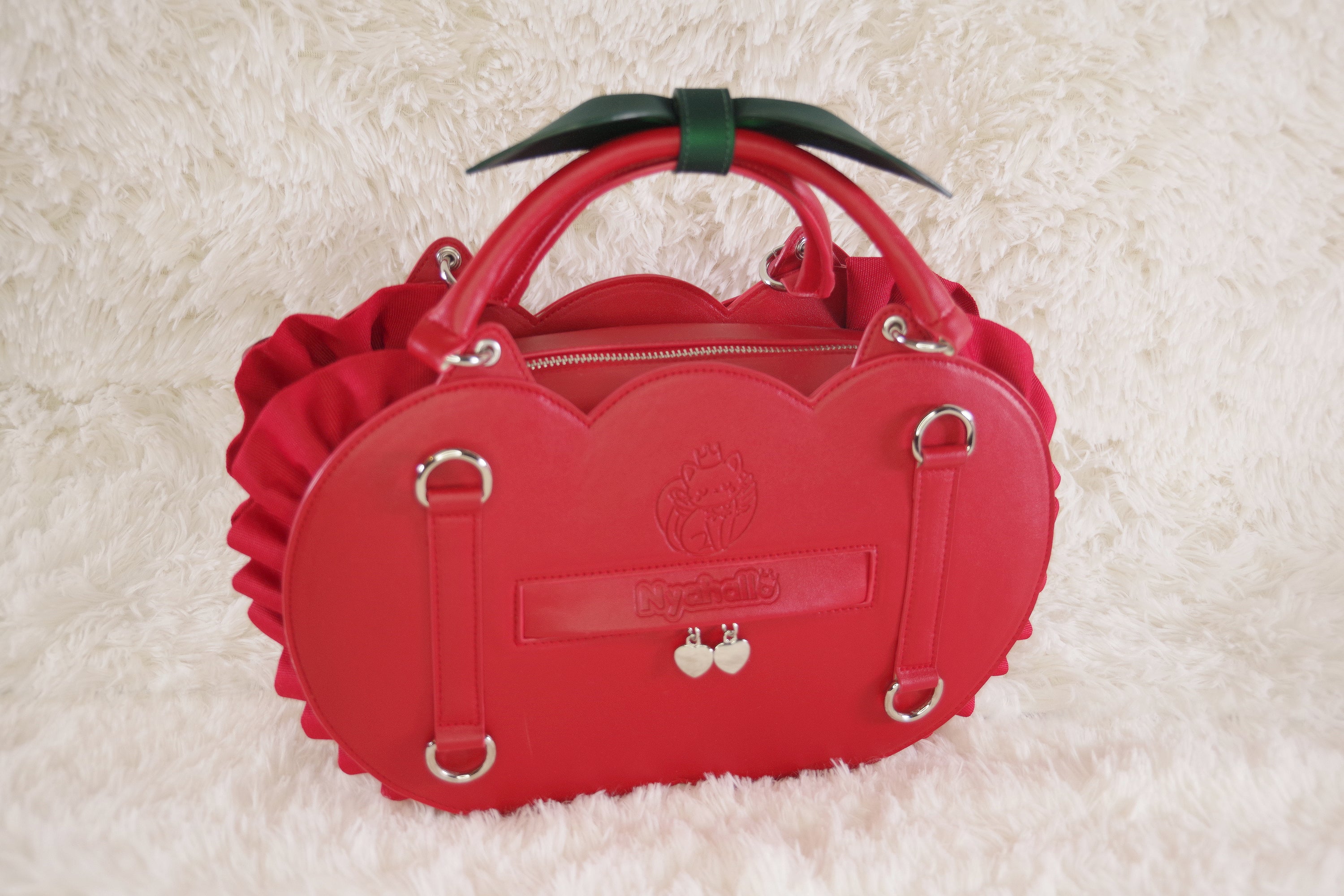 Back view of a cherry-inspired heart-shaped handbag featuring adjustable backpack straps, a rear slip pocket, cherry zipper charms, and a leaf-shaped handle accent.