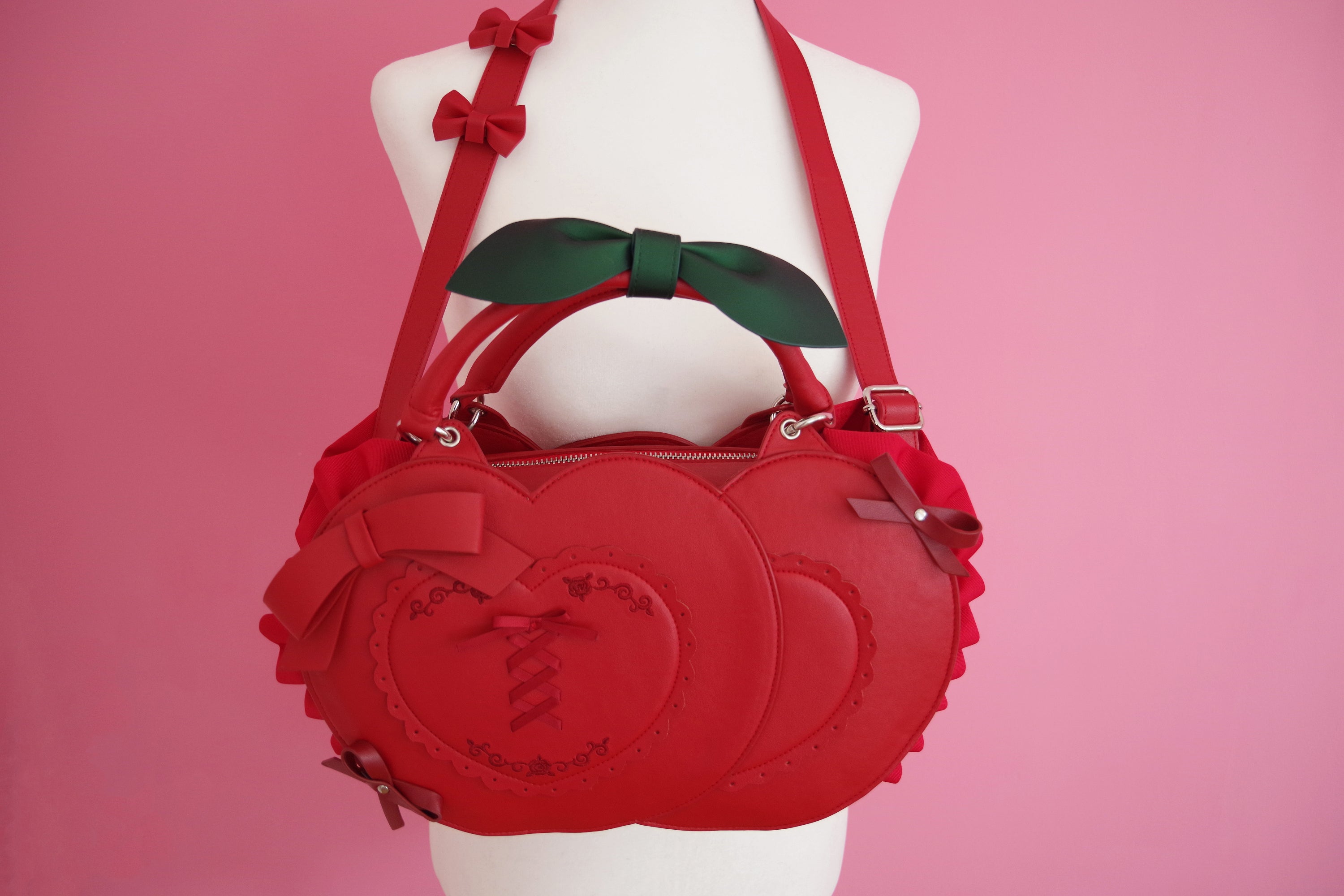 Frilly Fruits Cherry Purse featuring a cherry-inspired handbag design with layered heart panels, lace-up embroidery details, decorative bows, ruffled sides, adjustable shoulder strap, and removable leaf-shaped handle accent.