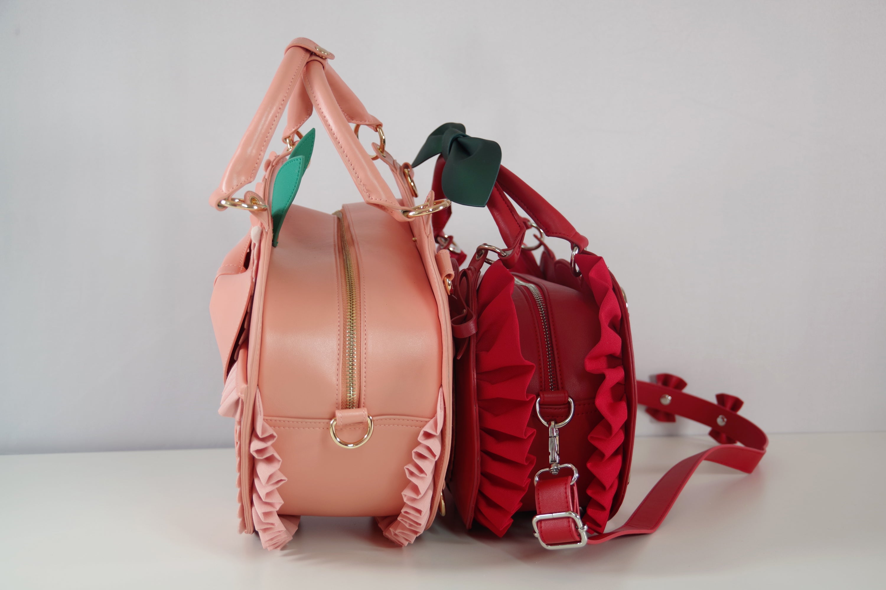 Side-by-side comparison of the Frilly Fruits Peach Purse and Cherry Purse, showing the profile view, ruffled fruit-inspired details, handles, and overall size differences.