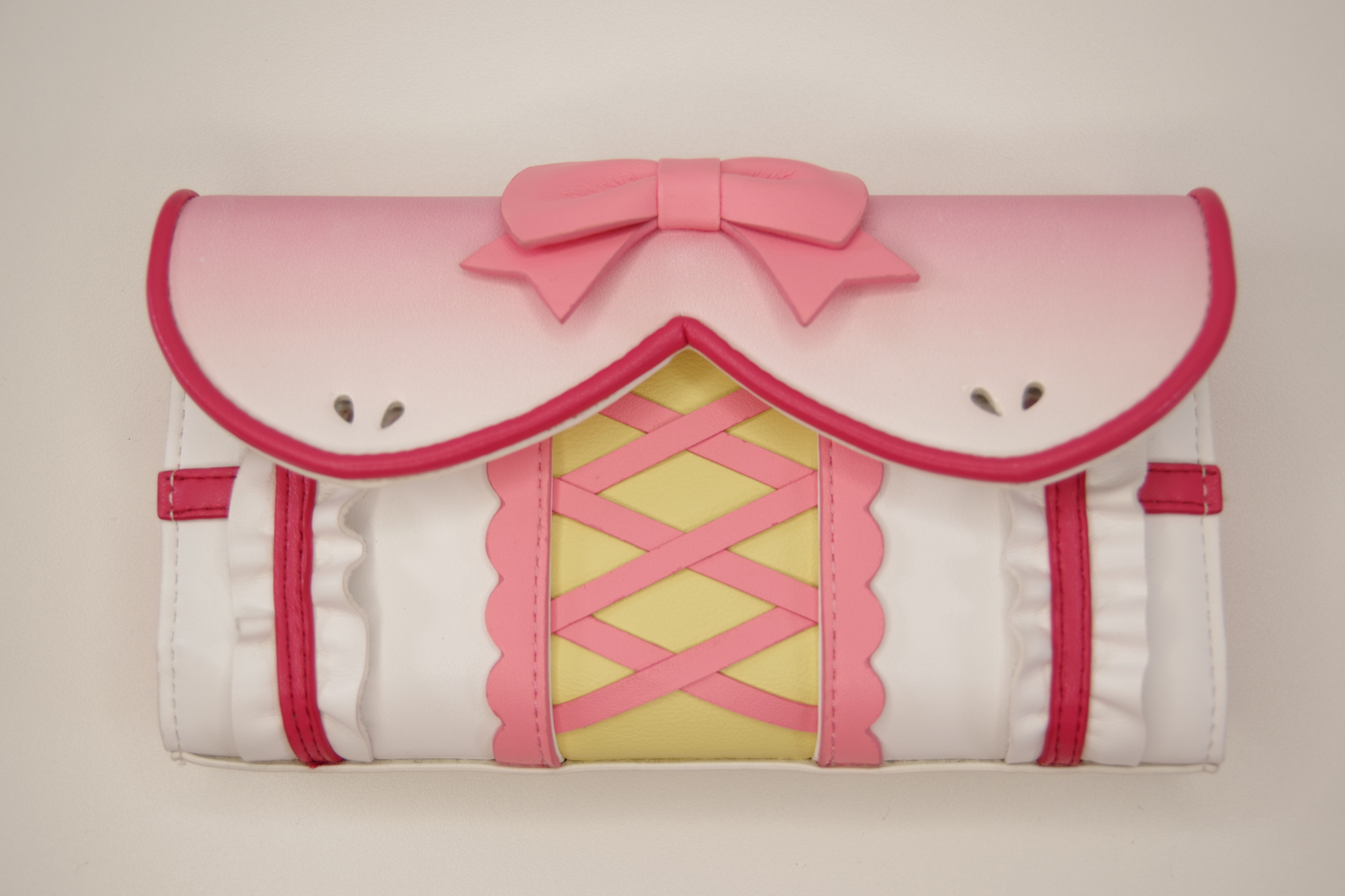 Front view of a pink magical girl inspired wallet featuring a bow accent, corset-style lacing, ruffle trim, and pastel kawaii design.