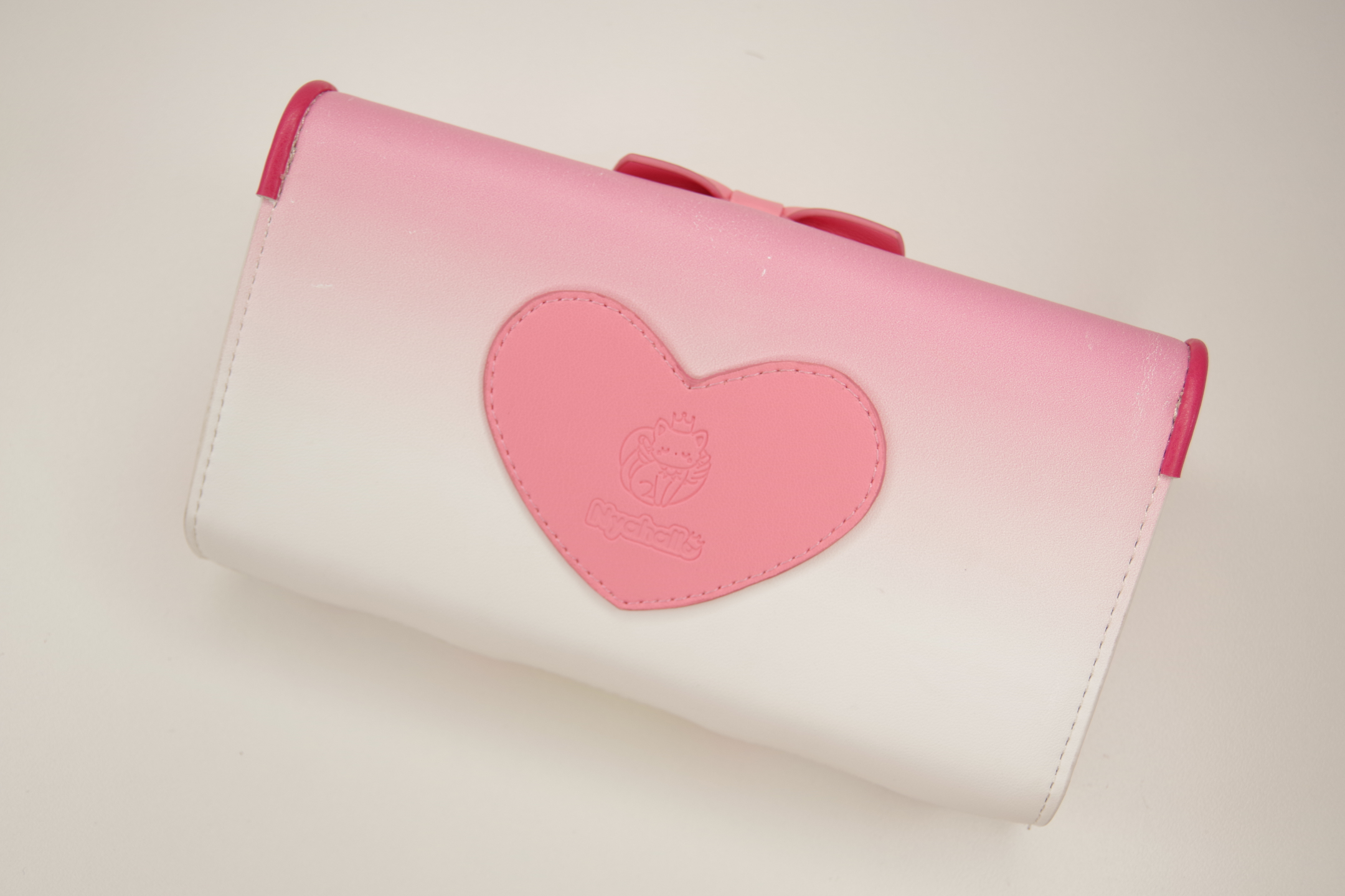 Angled back view of a pink magical girl inspired wallet featuring a heart-shaped logo applique and pastel pink to white gradient design.
