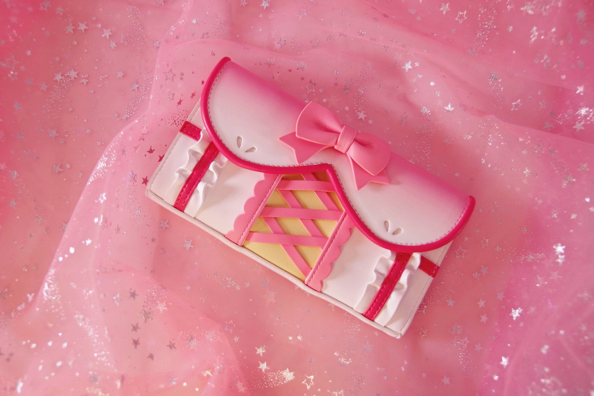 Pink magical girl inspired wallet featuring a large bow, corset lacing details, ruffles, and pastel kawaii fashion styling.